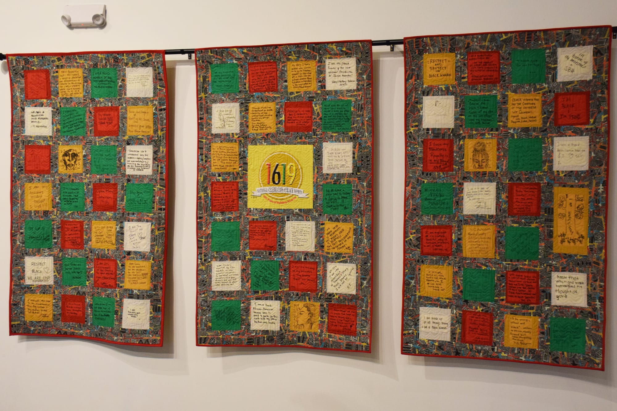 A panel of three quilts hangs on a wall