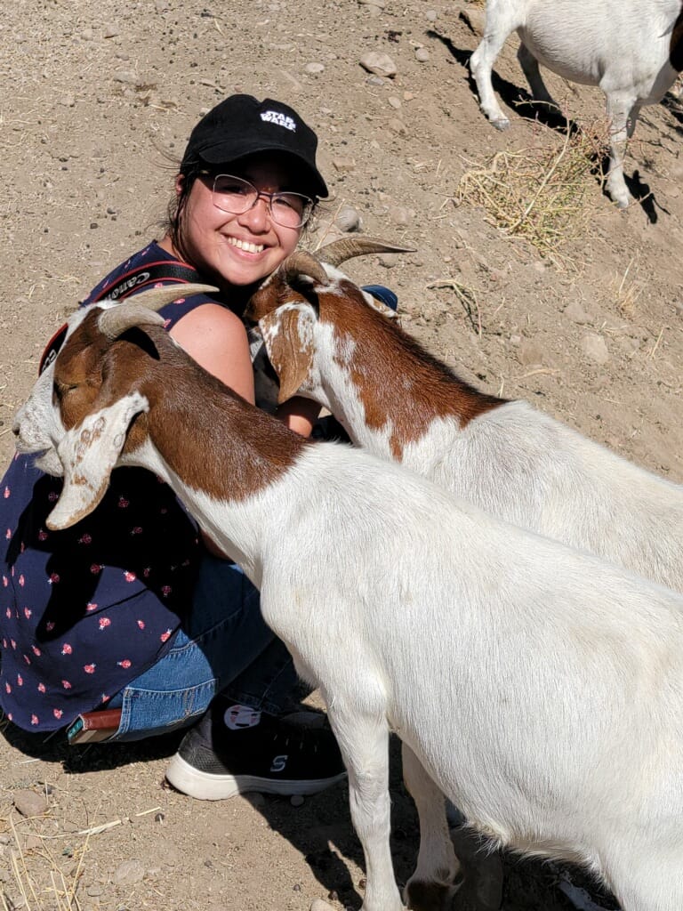 A woman squats down with two goats