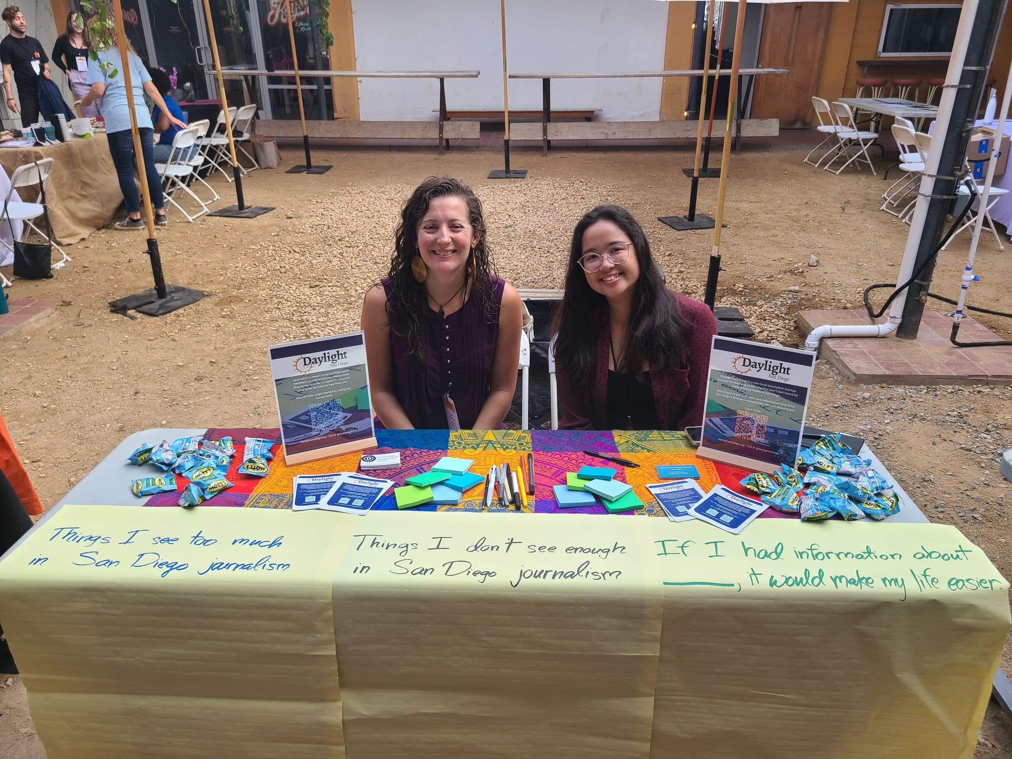 Two women sit at a table covered in post-it notes and signs at an event