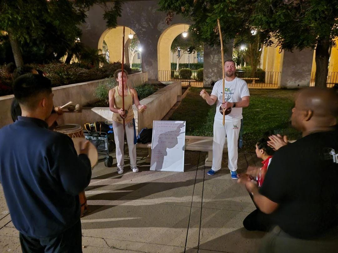 Two people stand in front of a crowd teaching a capoeira class