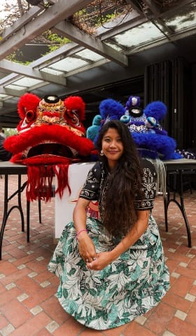 Photo of a woman crouching in front of two large lion dancer heads