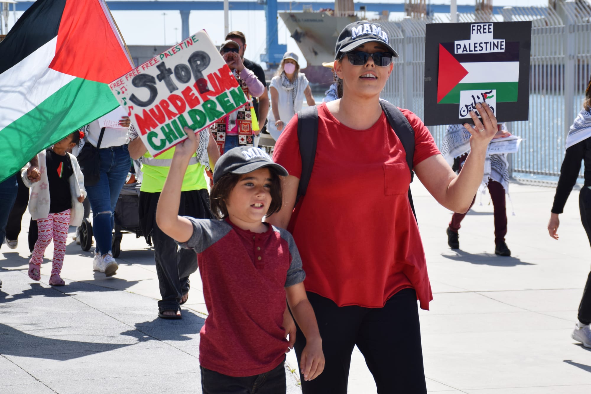 A boy holds a sign that reads "free free Palestine" and "stop murdering children" next to his mom holding a sign that reads "free palestine"