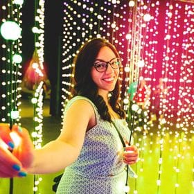 Photo of a woman in front of a wall of hanging twinkle lights.