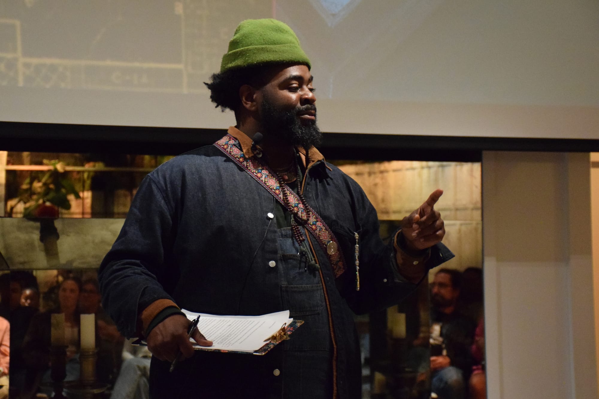 A man in a green beanie and denim jacket holds a clip board