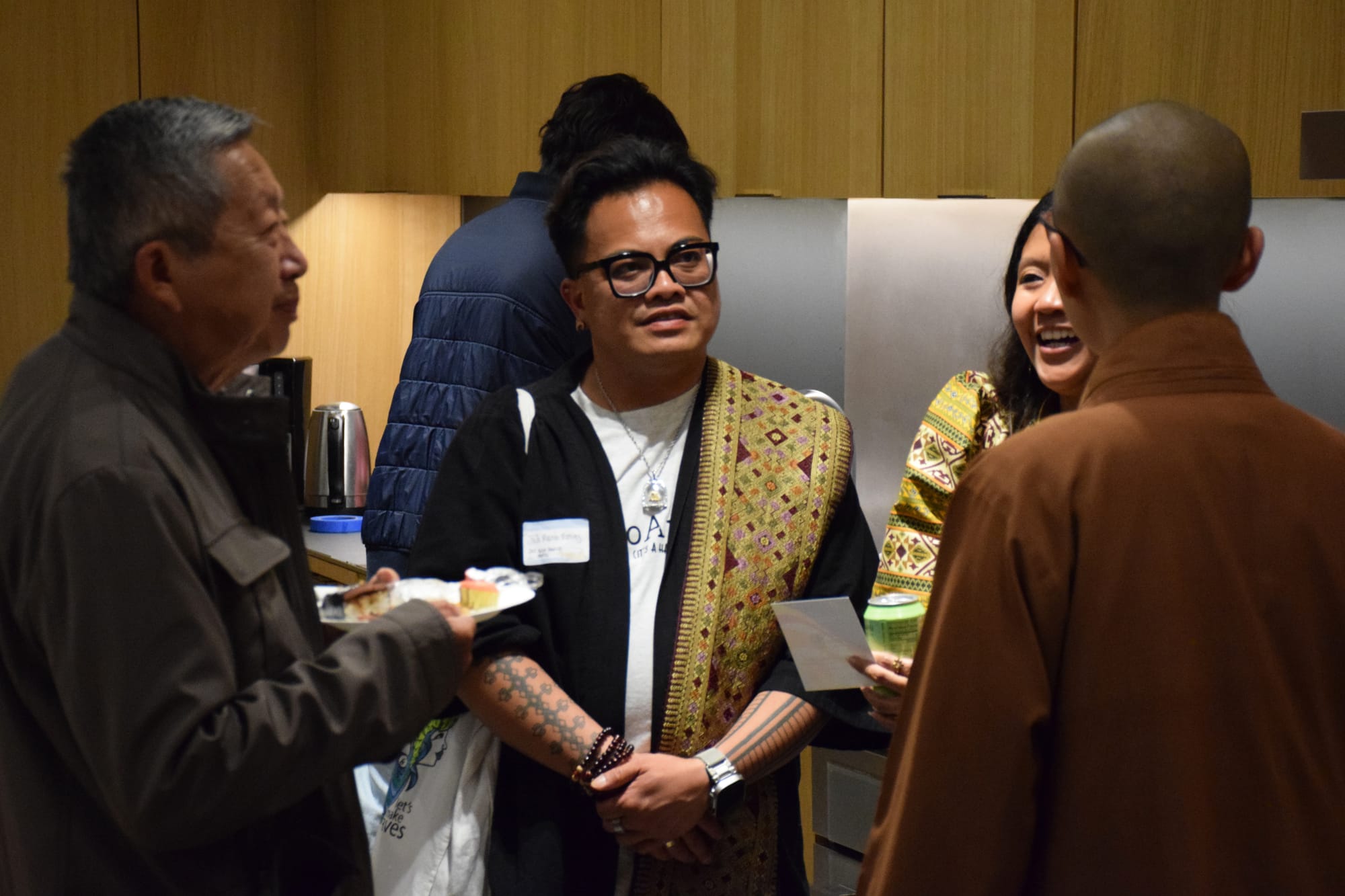 Four people speak to one another in front of a kitchen while someone else works in the background