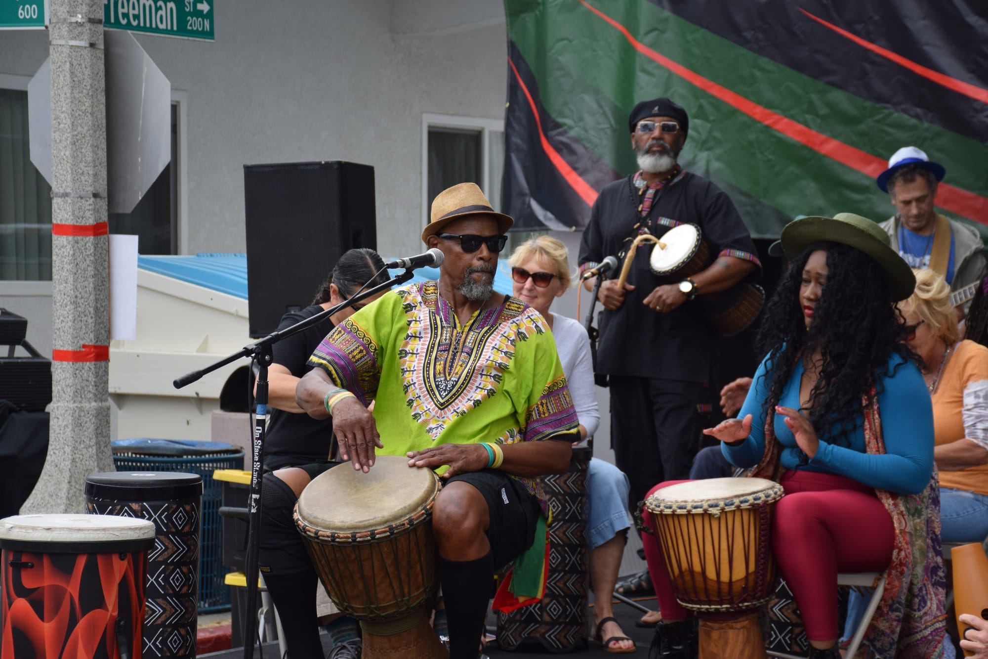 a group sits on the stage of an outdoor event performing with african drums