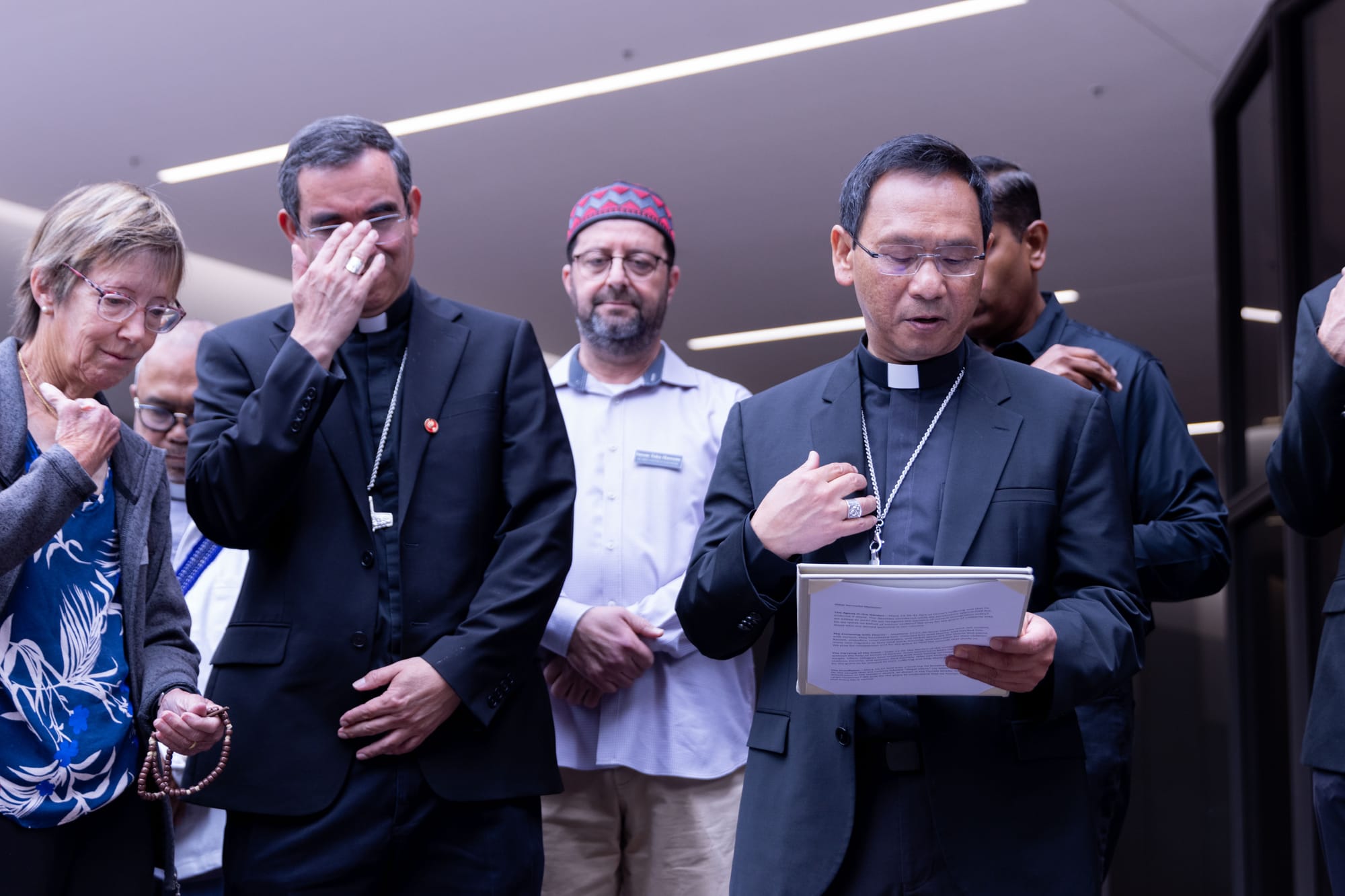 A group of people stand together, some holding rosary beads.