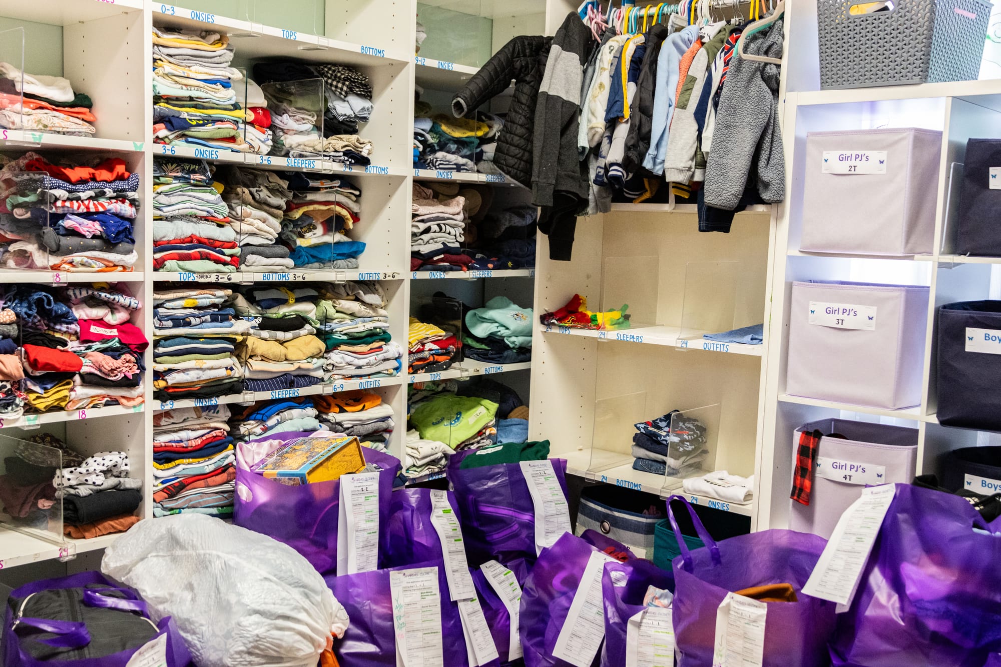 A closet features shelves of baby clothing and purple bags with orders pinned to them.