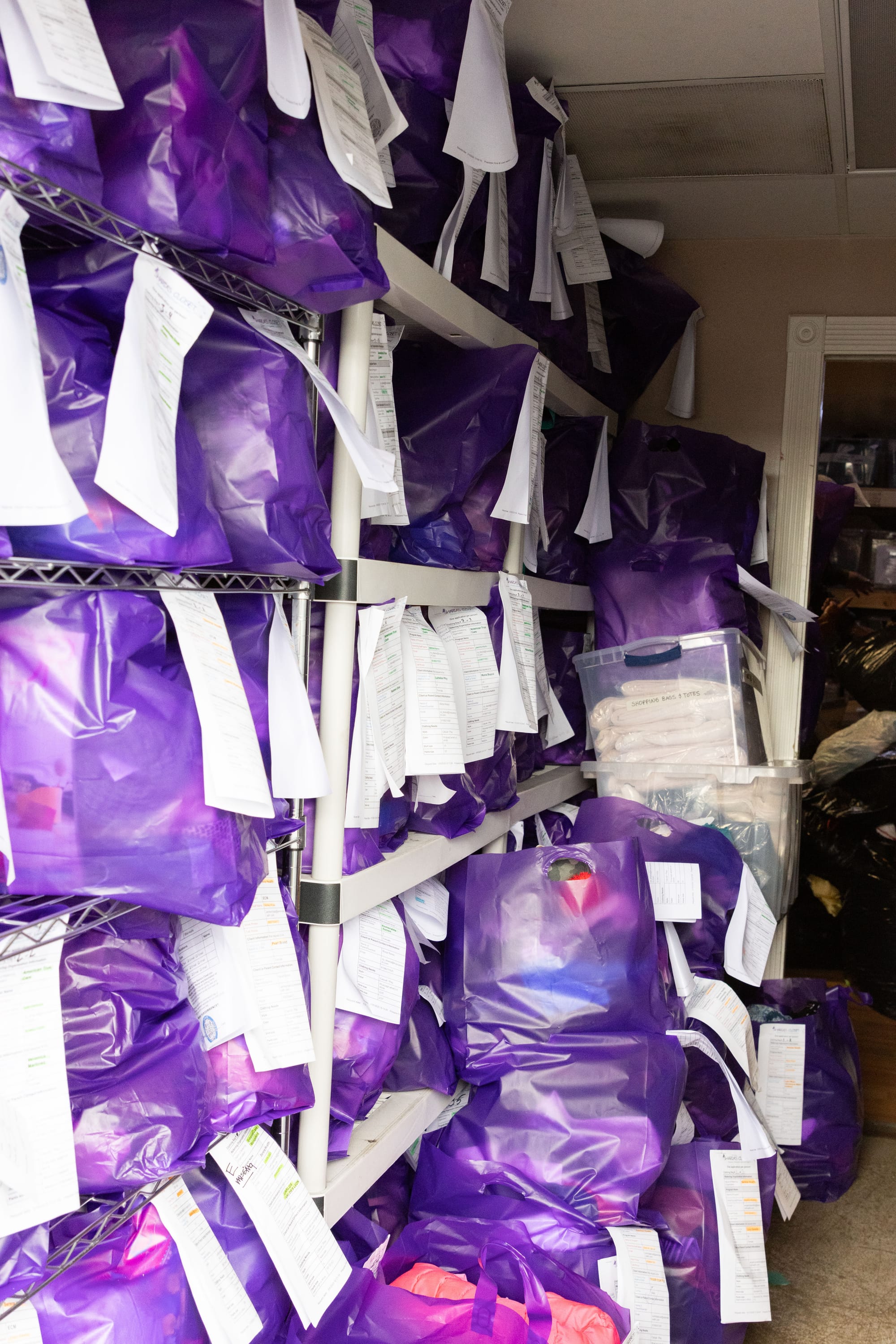 Purple bags filled with clothes and pinned with order forms are stacked on shelves