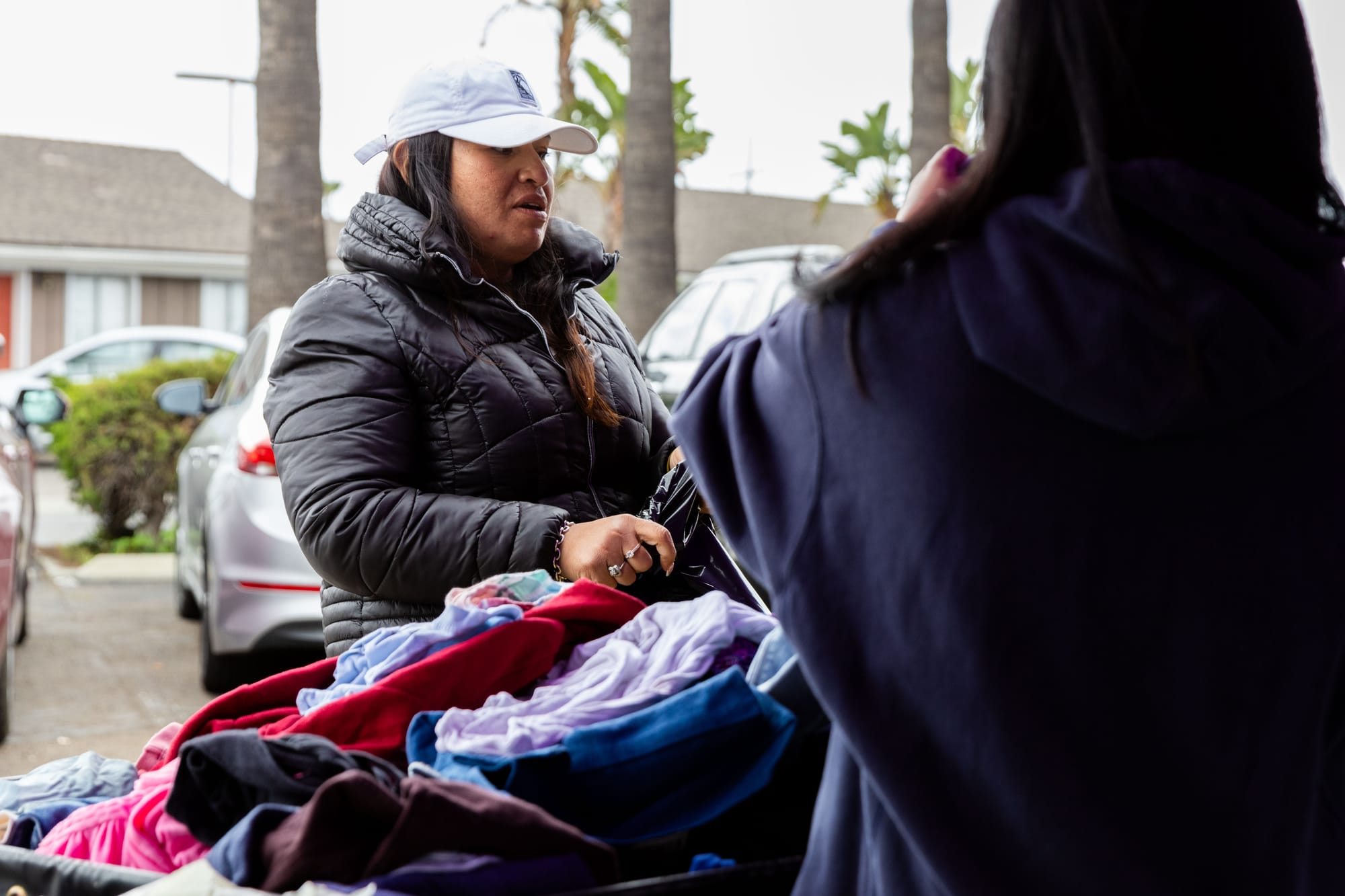A woman in a puffy coat and hat sorts clothing at an outdoor event