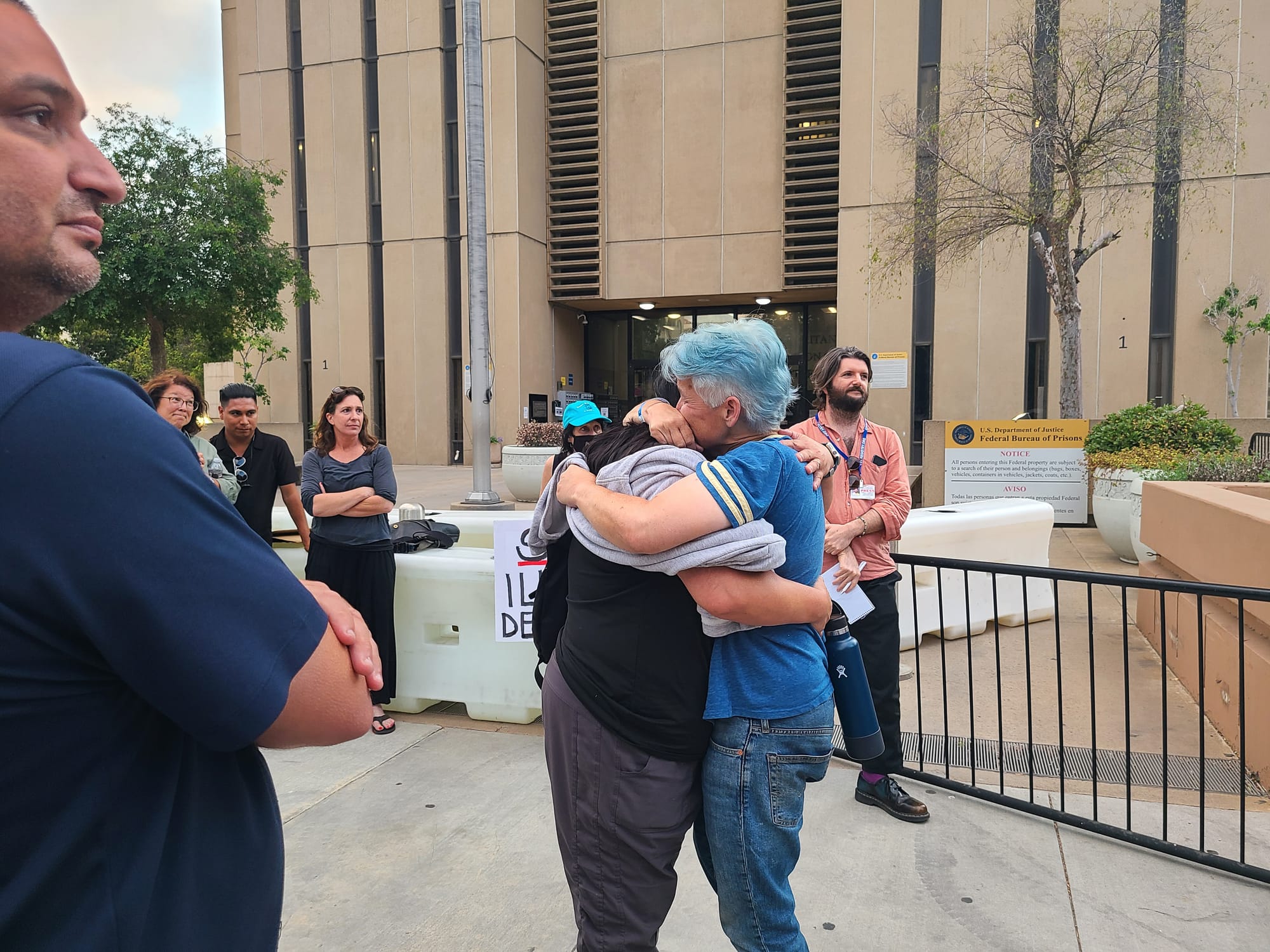 A woman hugs her wife outside among other people.