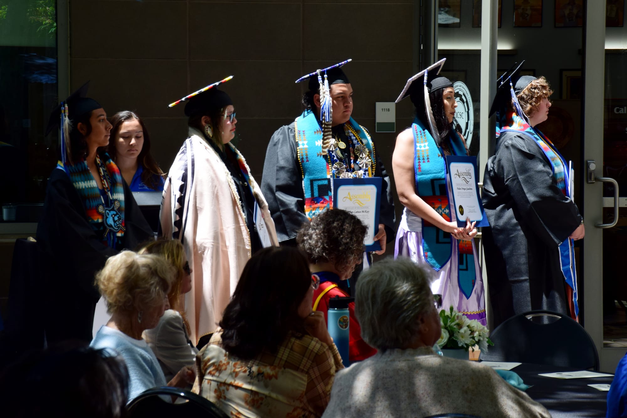 A group of graduates stand in front of people at a luncheon outside