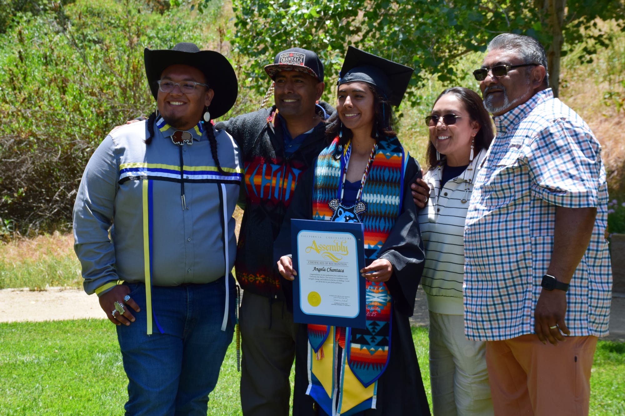A family poses for a photo outside with a person in graduation regalia at the center