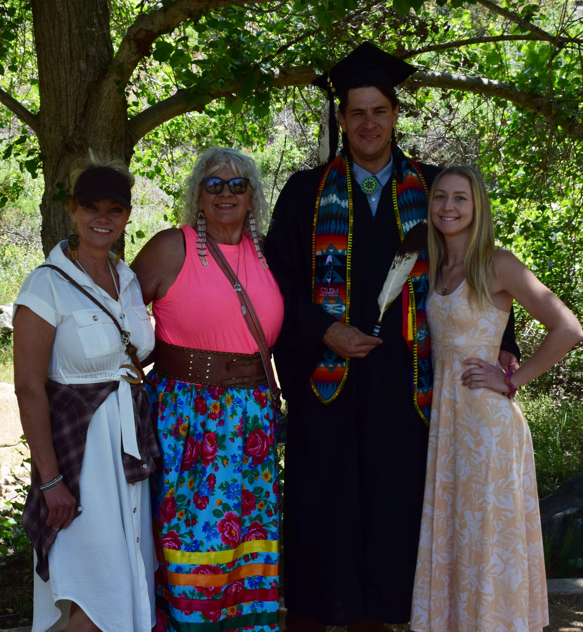 A graduating student stands under a tree with three women