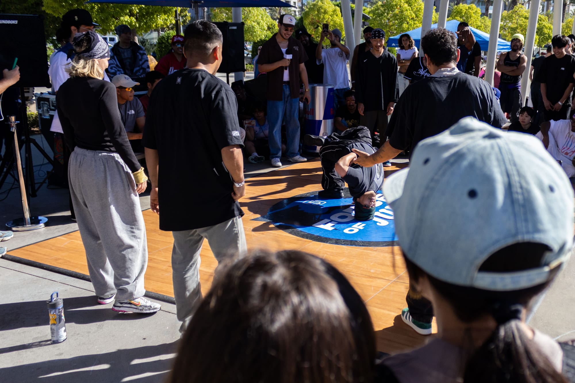A dancer performs in a breaking competition in a crowd outside in a park.
