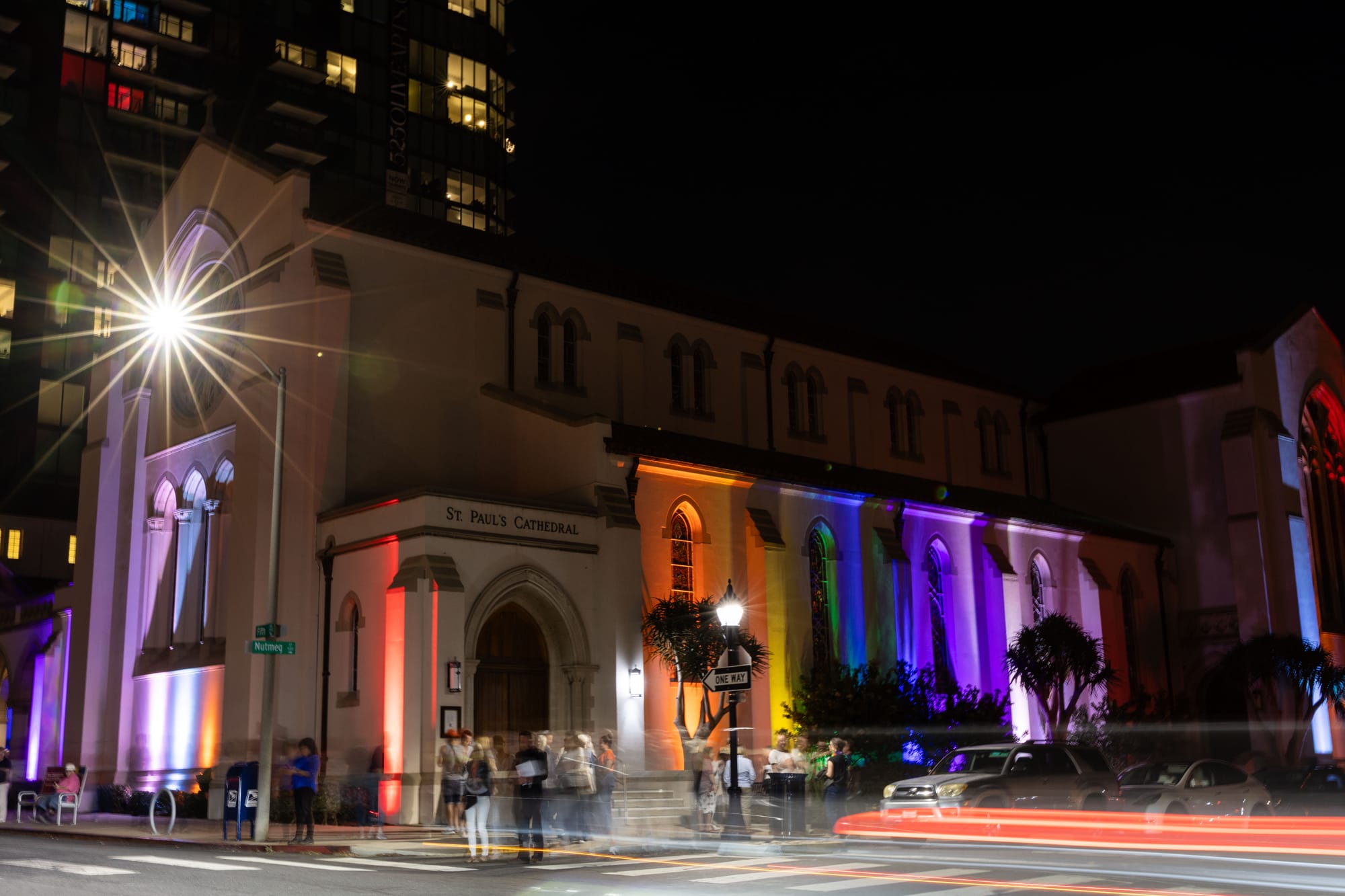 Light shines on the window of a church while rainbow lights light up its sides.