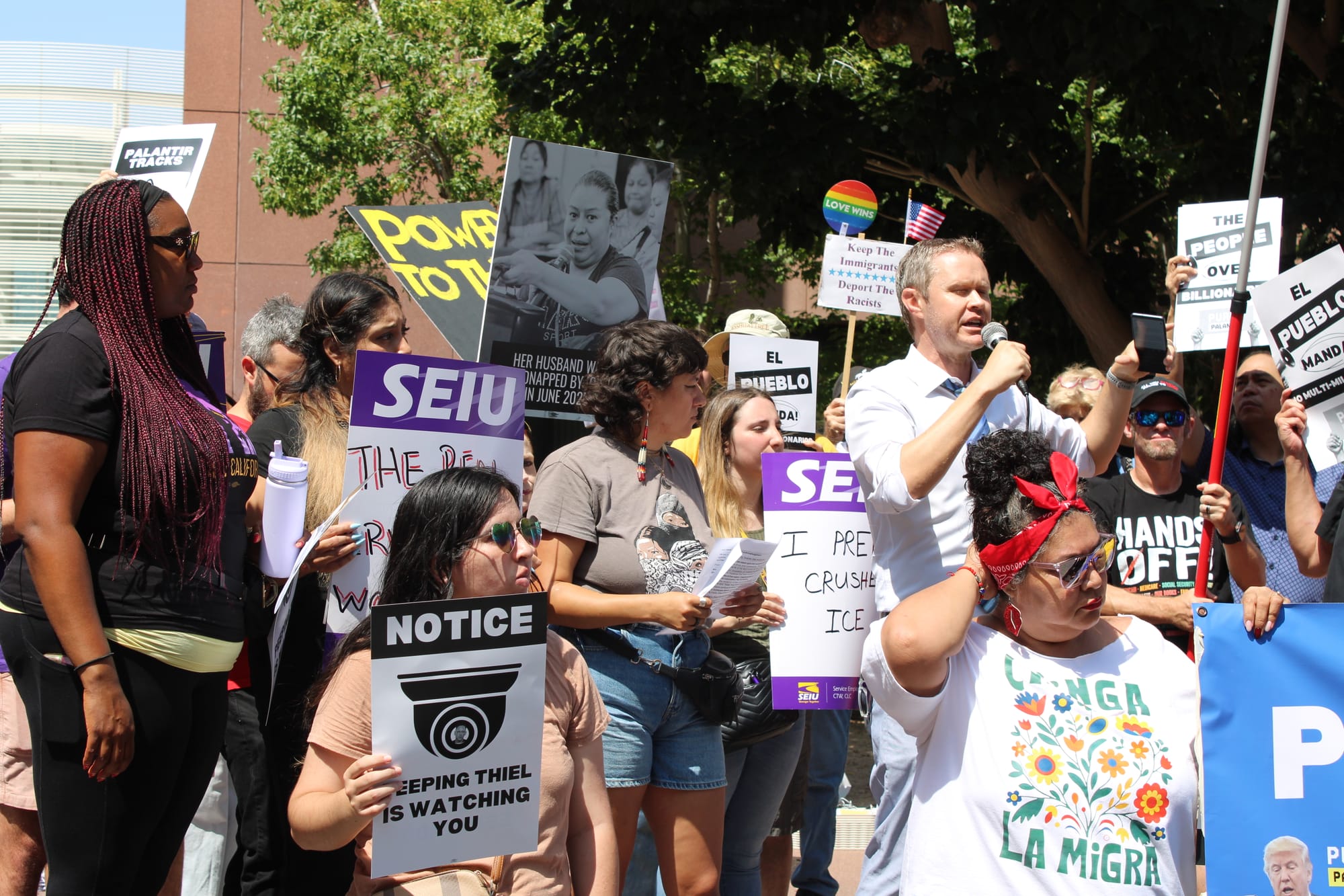 A man speaks into a microphone in the center of a crowd of protesters 