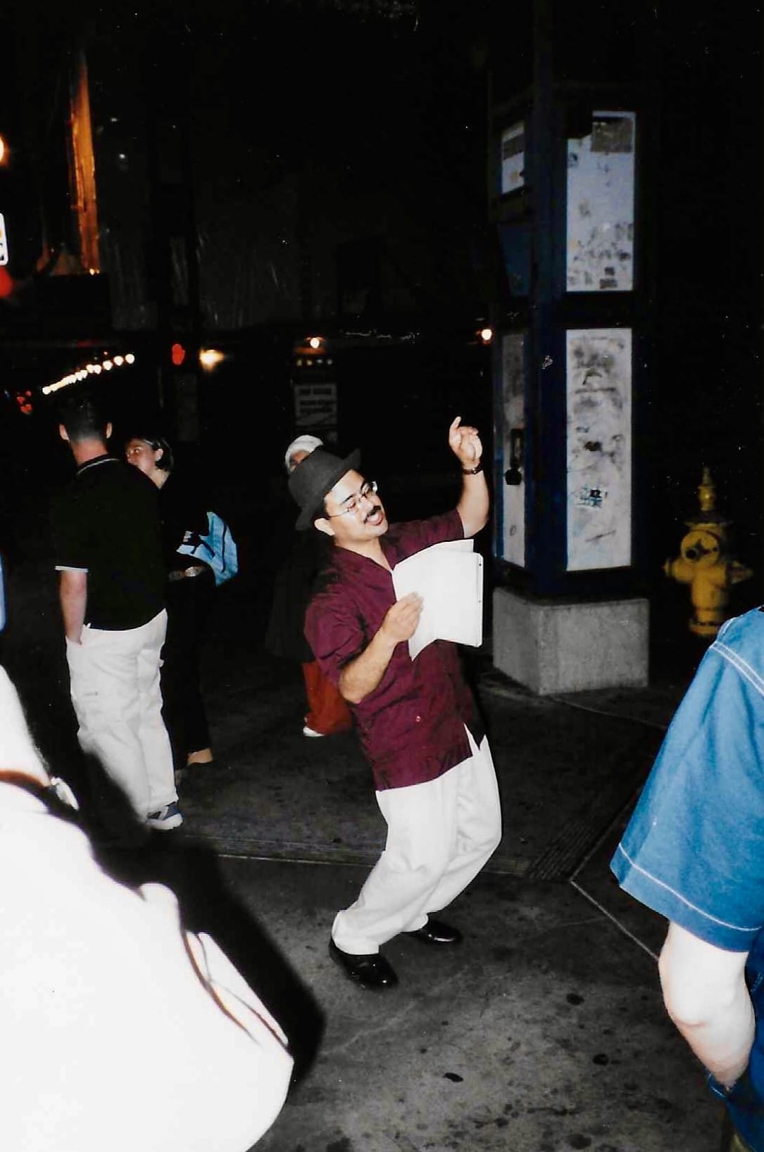 A poet reads a piece of their work outside at night with other people around them