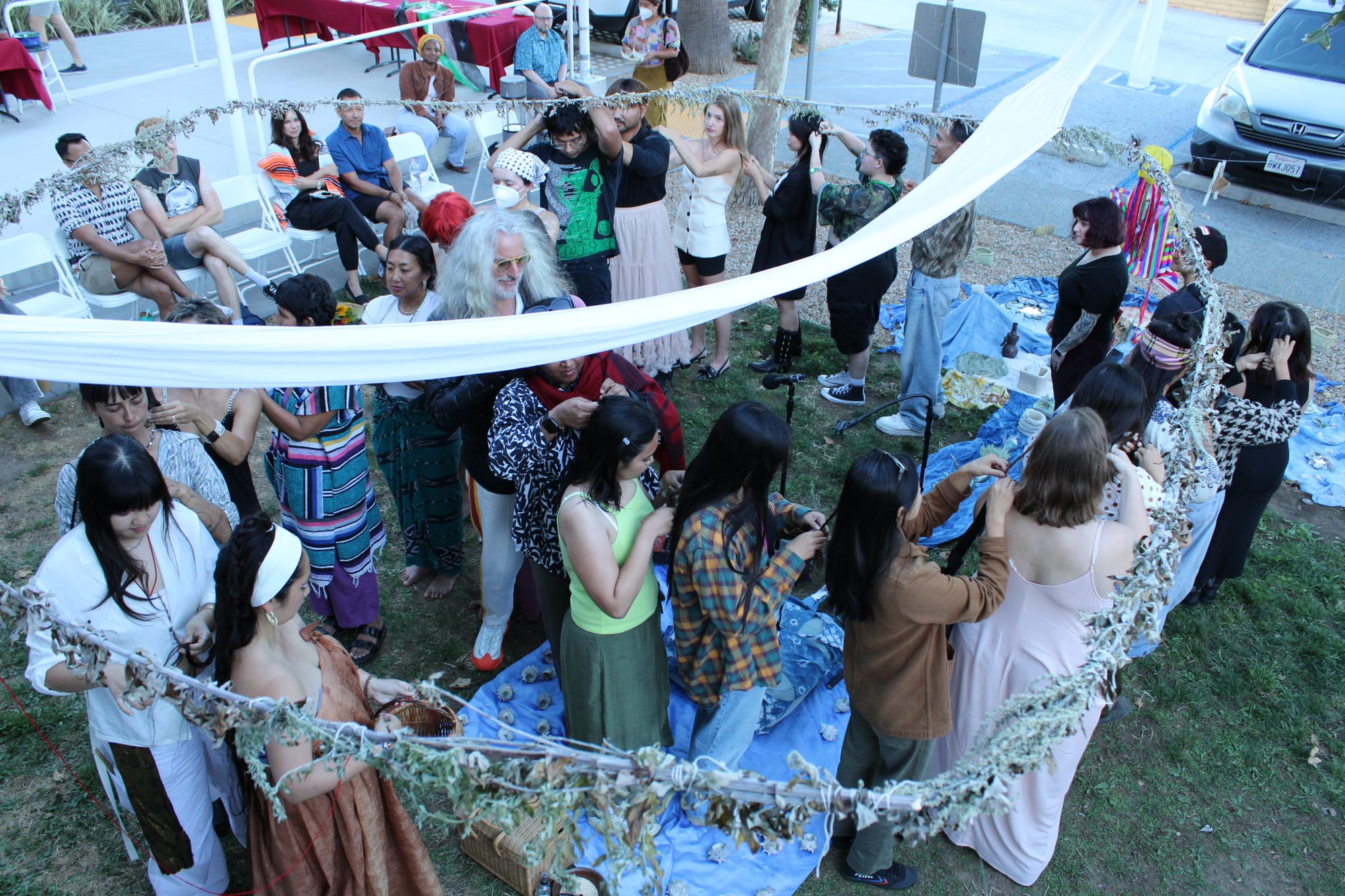people stand in a spiral braiding one another's hair