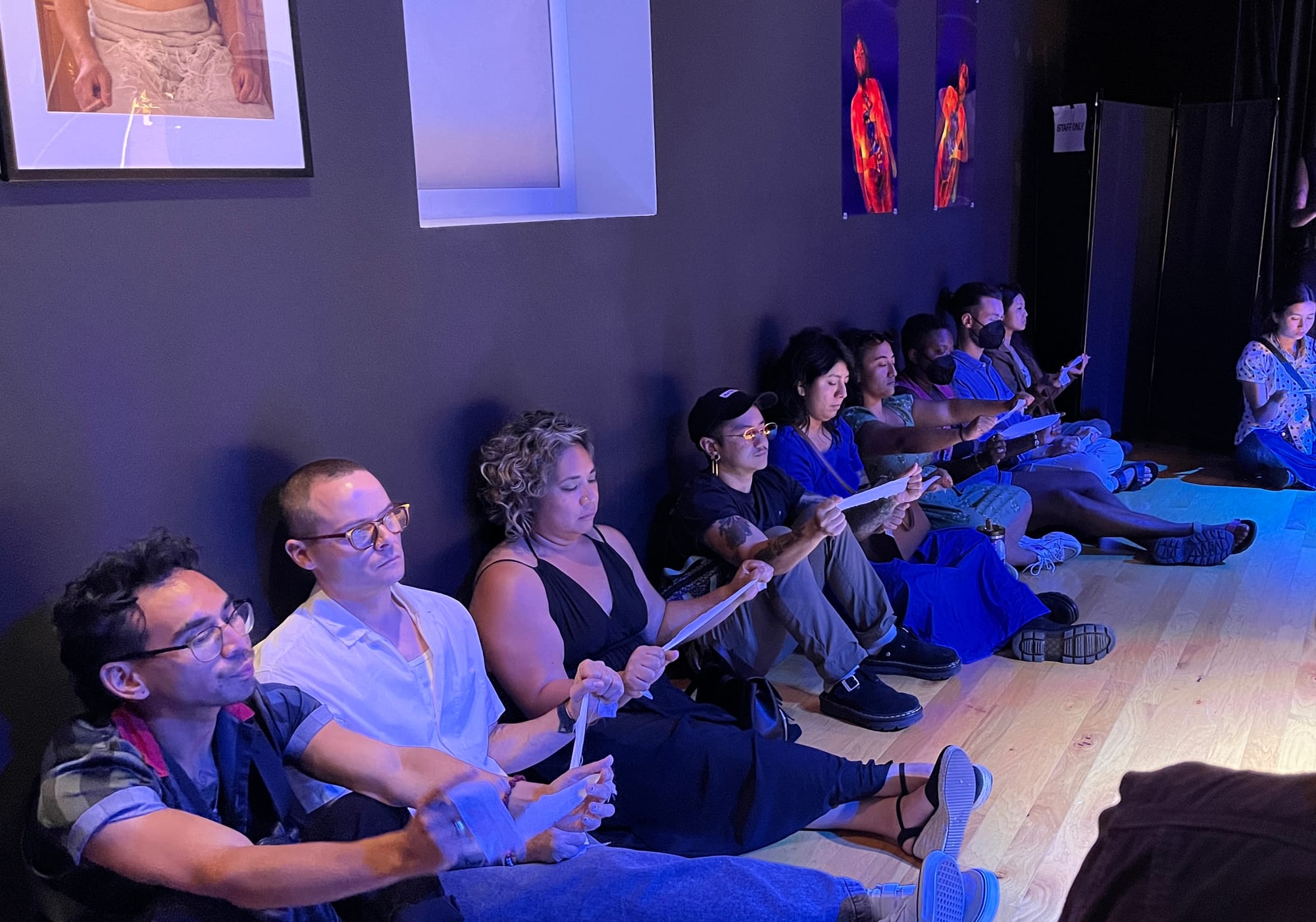 People sit on the floor next to each other holding strips of cloth out