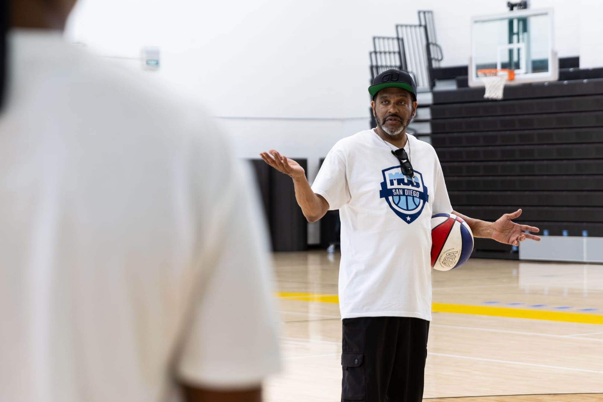A coach talks while holding a basketball under his arm in a gym