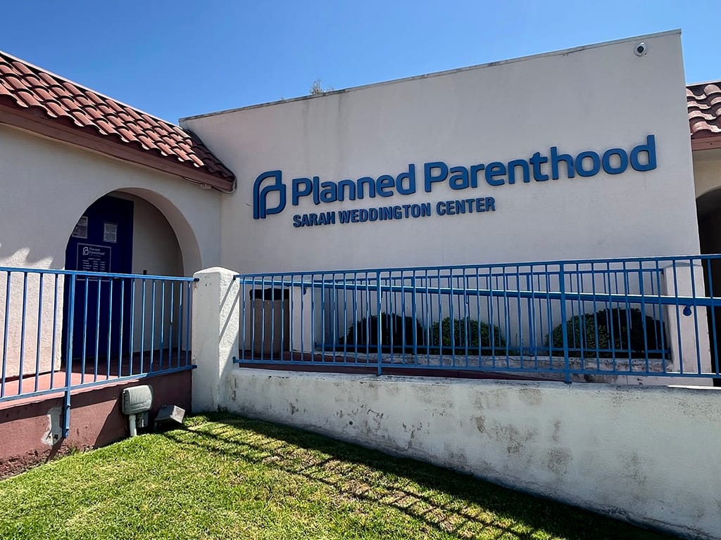 Picture of the outside of a Planned Parenthood clinic that says "Planned Parenthood Sarah Weddington Center" in blue lettering on the side