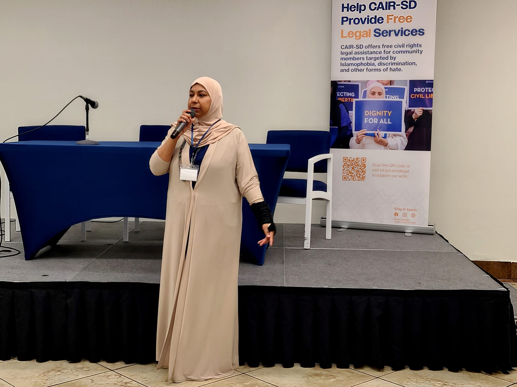 A woman wearing hijab speaks into a microphone at a conference