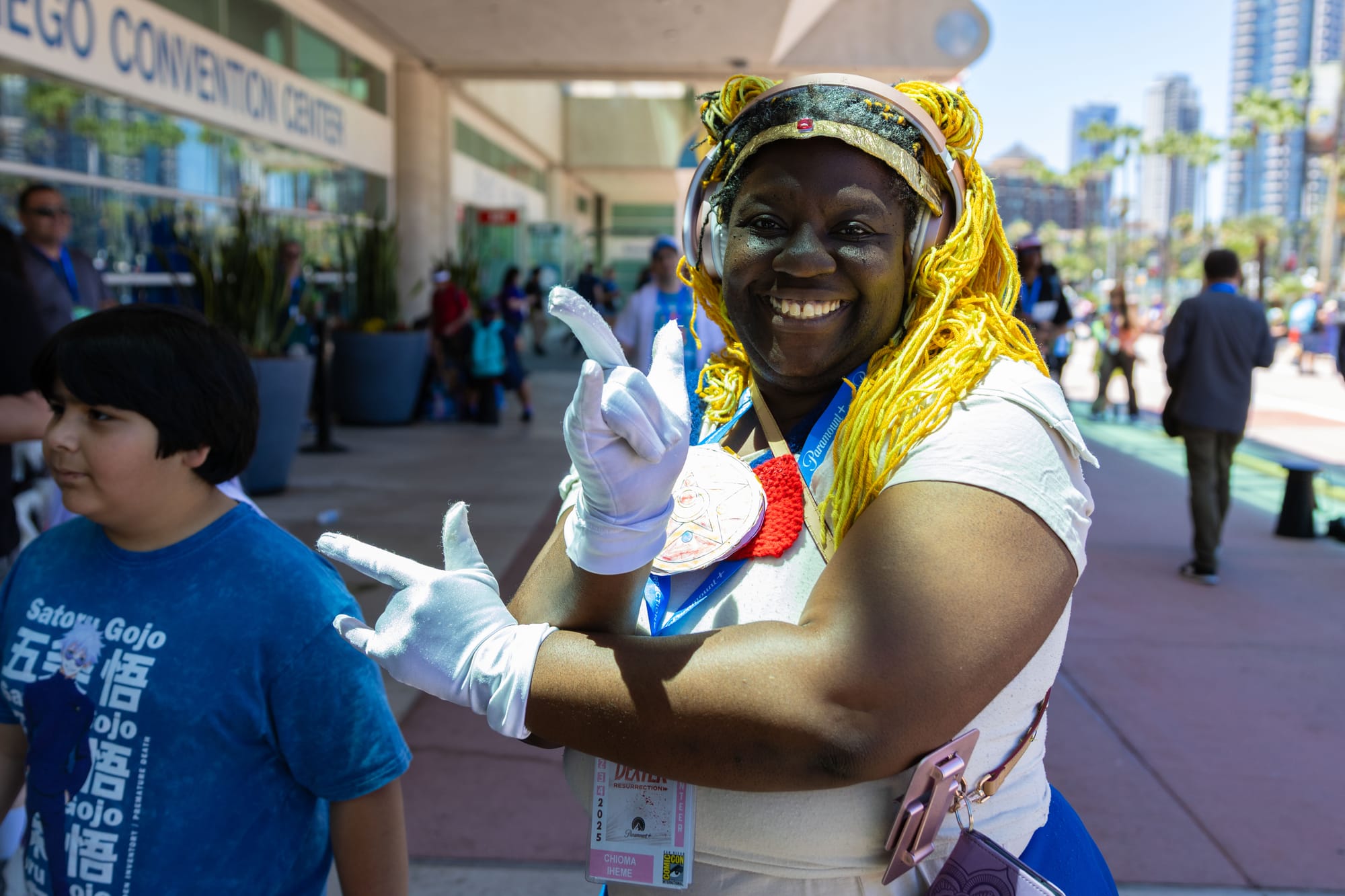 A person dressed in a sailor moon cosplay poses for a photo outside of a convention center with people walking behind her
