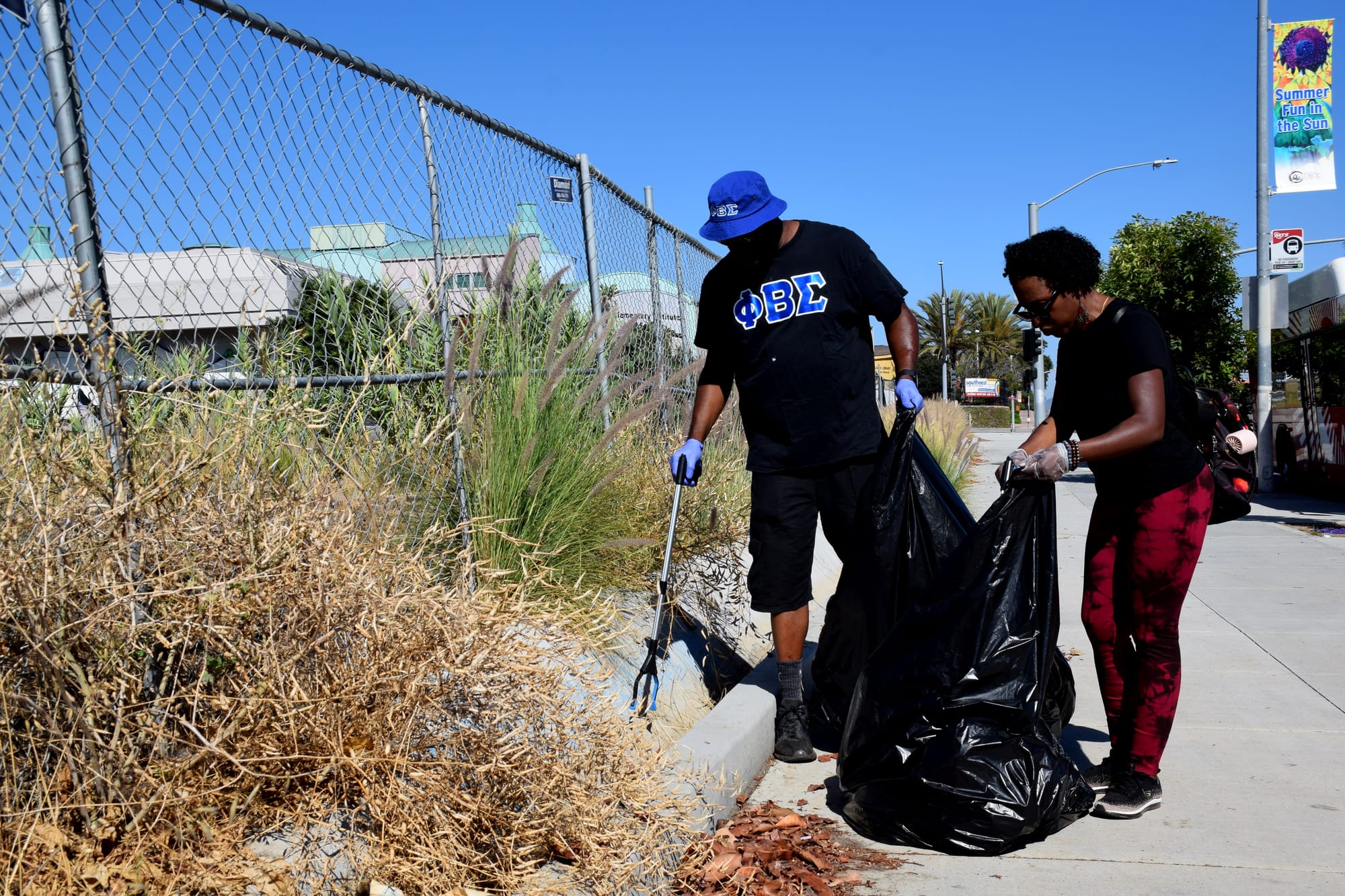 A man and a woman fill a trash bag with garbage