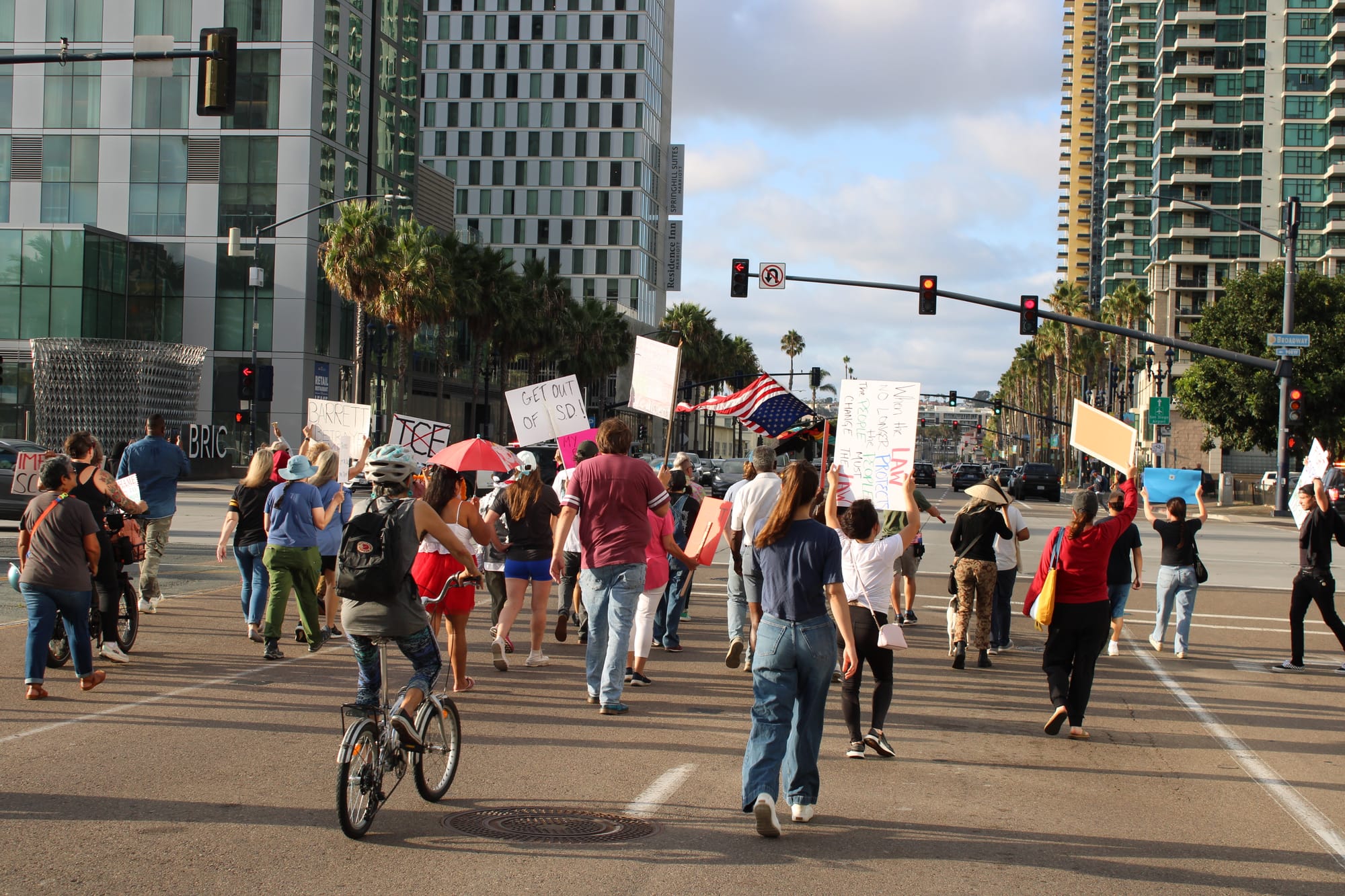 Image of people walking and riding bikes in a protest down a california street holding picket signs