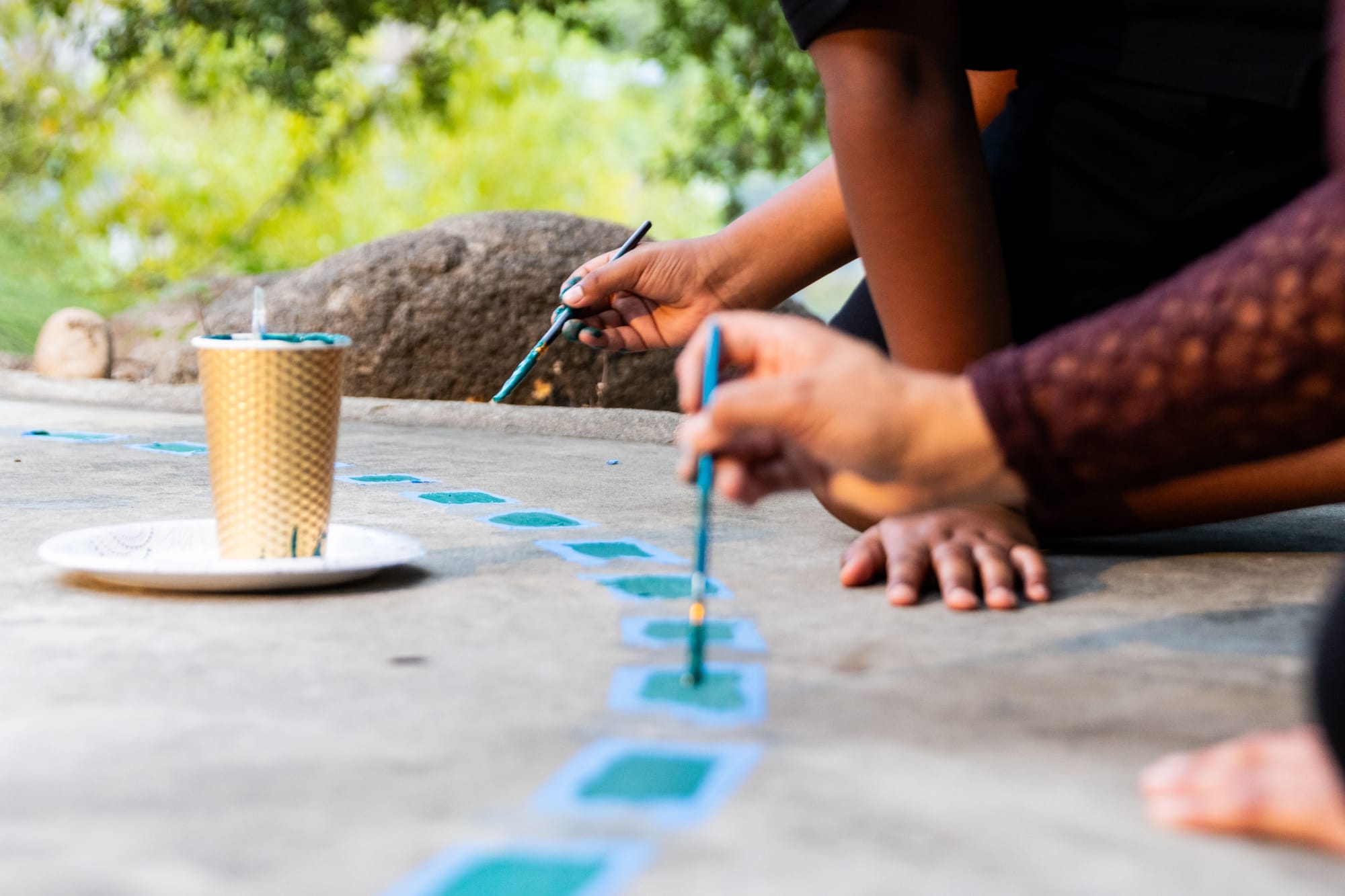 A close up of peoples hands as they paint a calendar on the ground
