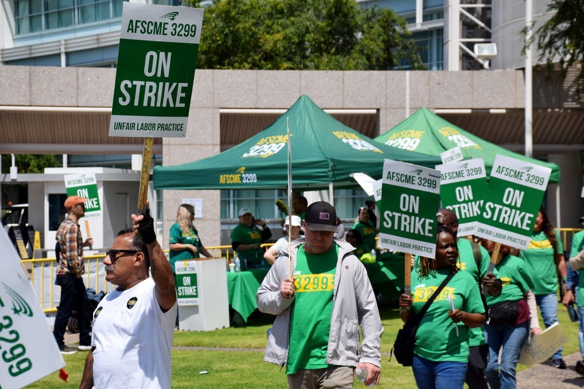 People hold picket signs that read AFSCME 3299 On Strike Unfair Labor Practice outside