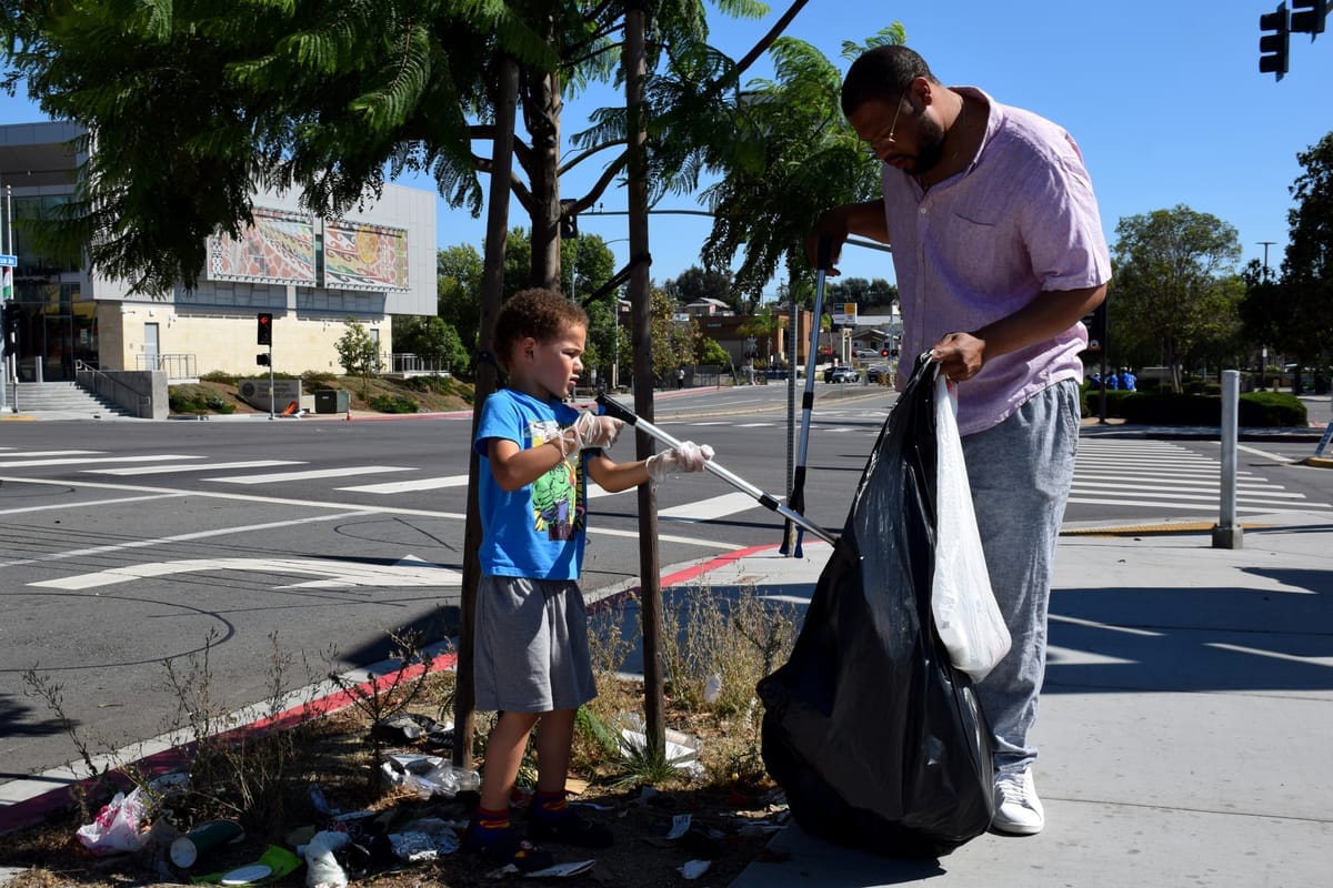 A boy and a man pick up trash next to a street