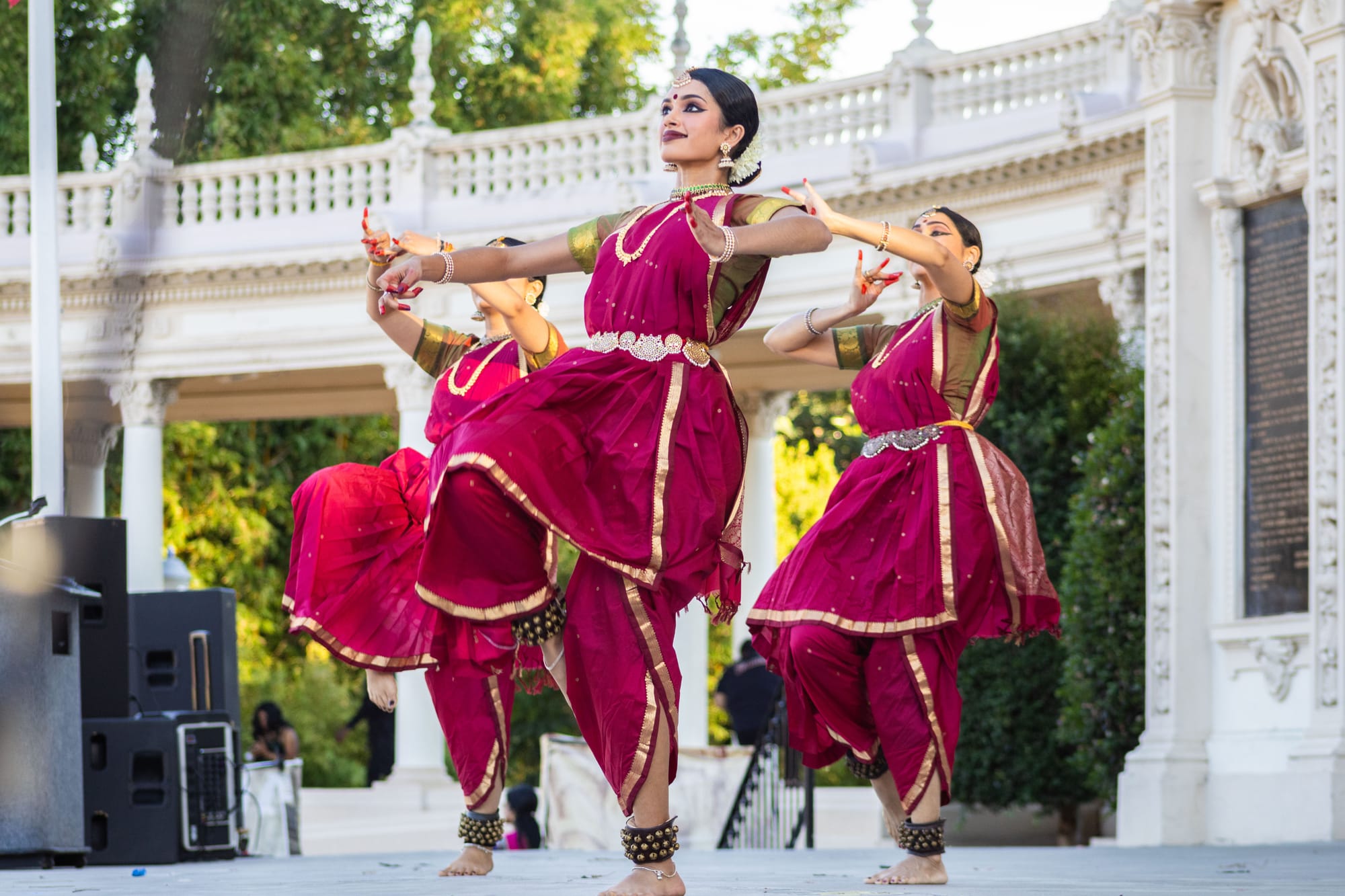 Three women in red dance with their hands in front of them and one leg bent up. 