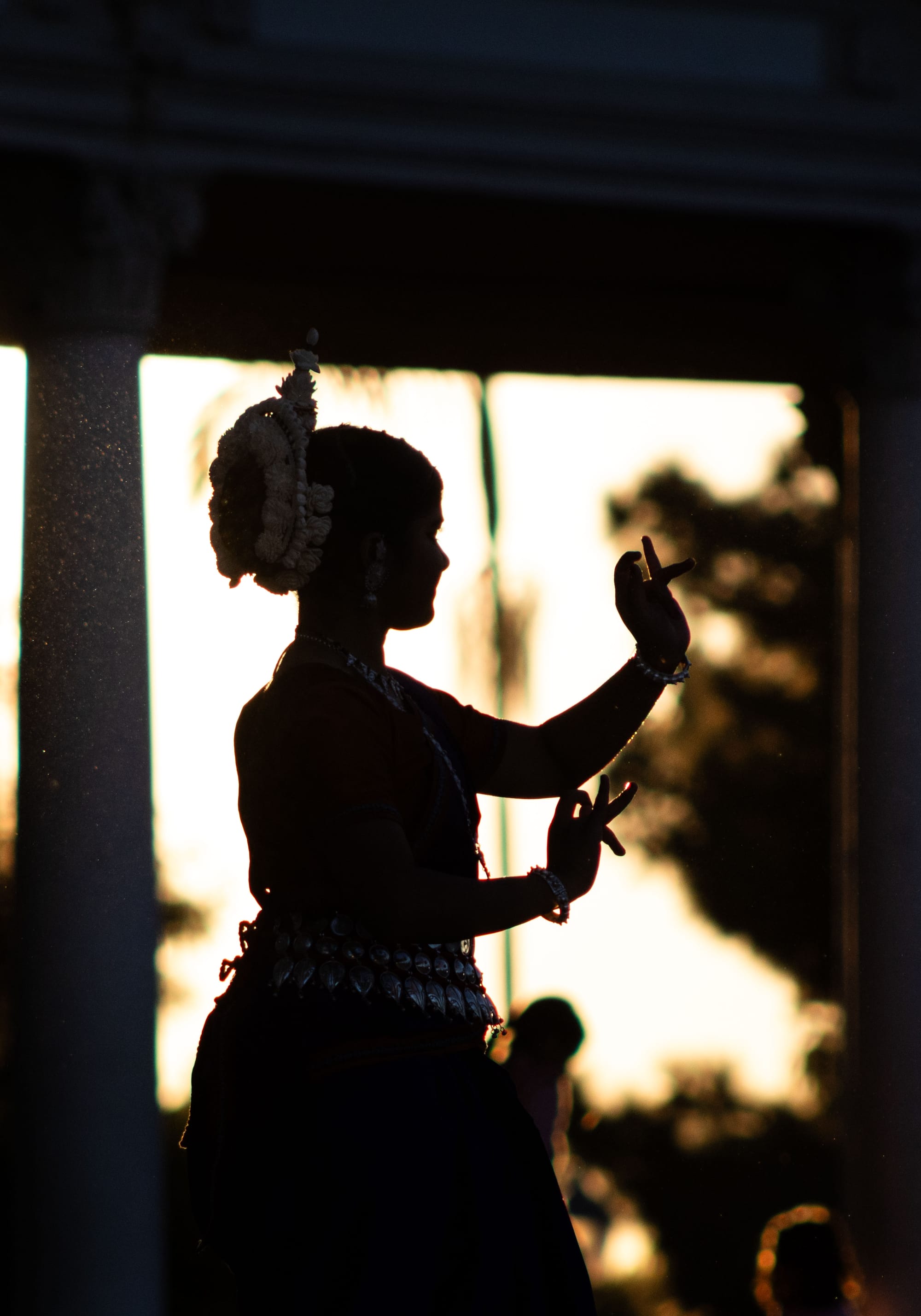 A woman is silhouetted against the sun while holding her hands up during a dance.  