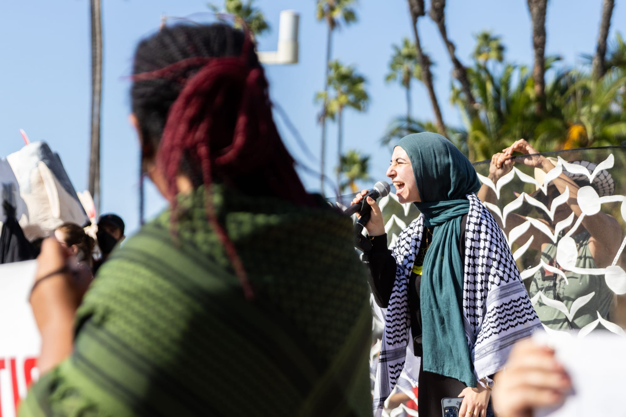 A woman in hijab shouts into a microphone in a crowd during a demonstration outside