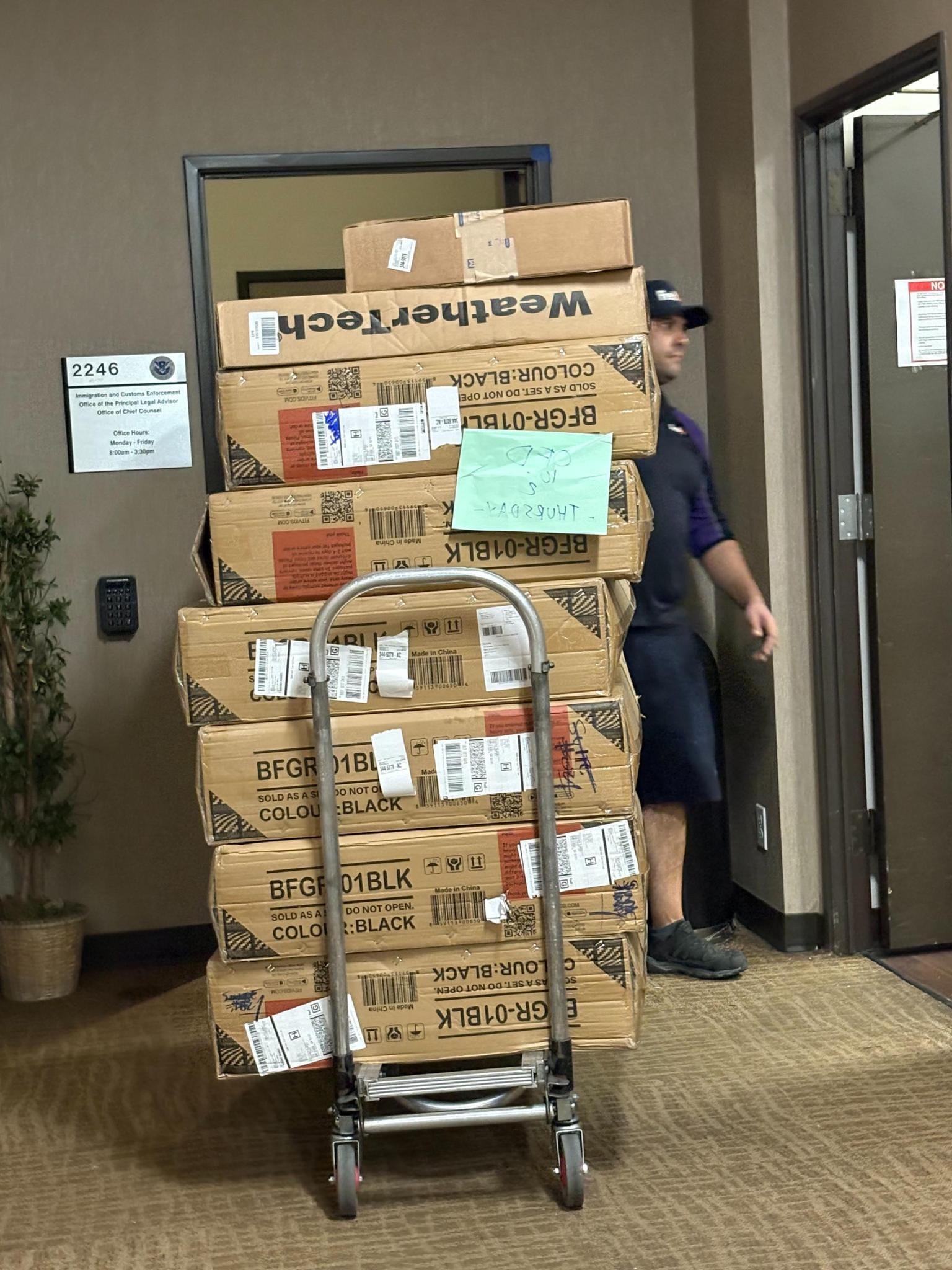 A delivery person stands with a dolly cart full of boxes