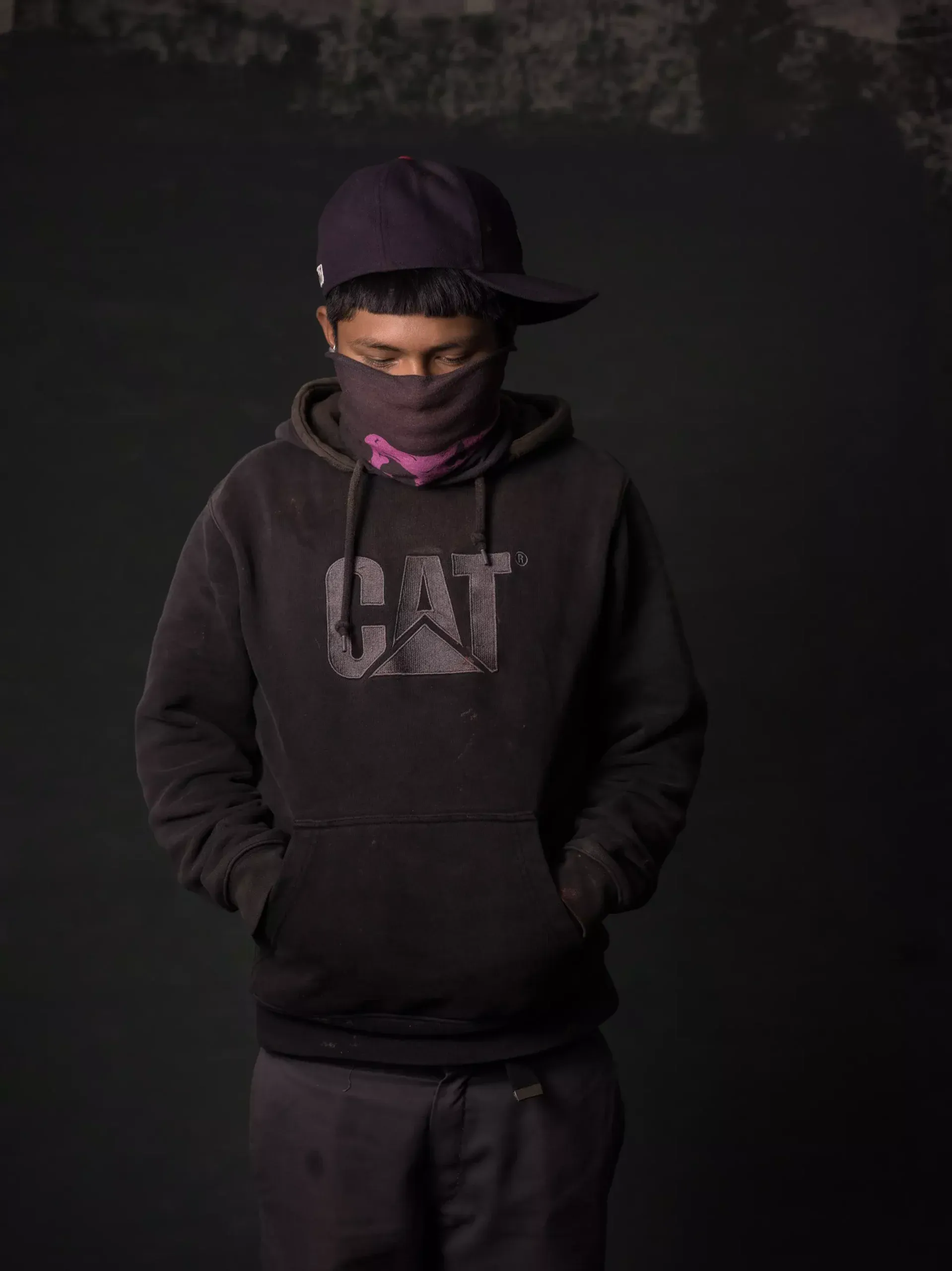 A boy wears a black hat and purple bandana as he looks at the floor