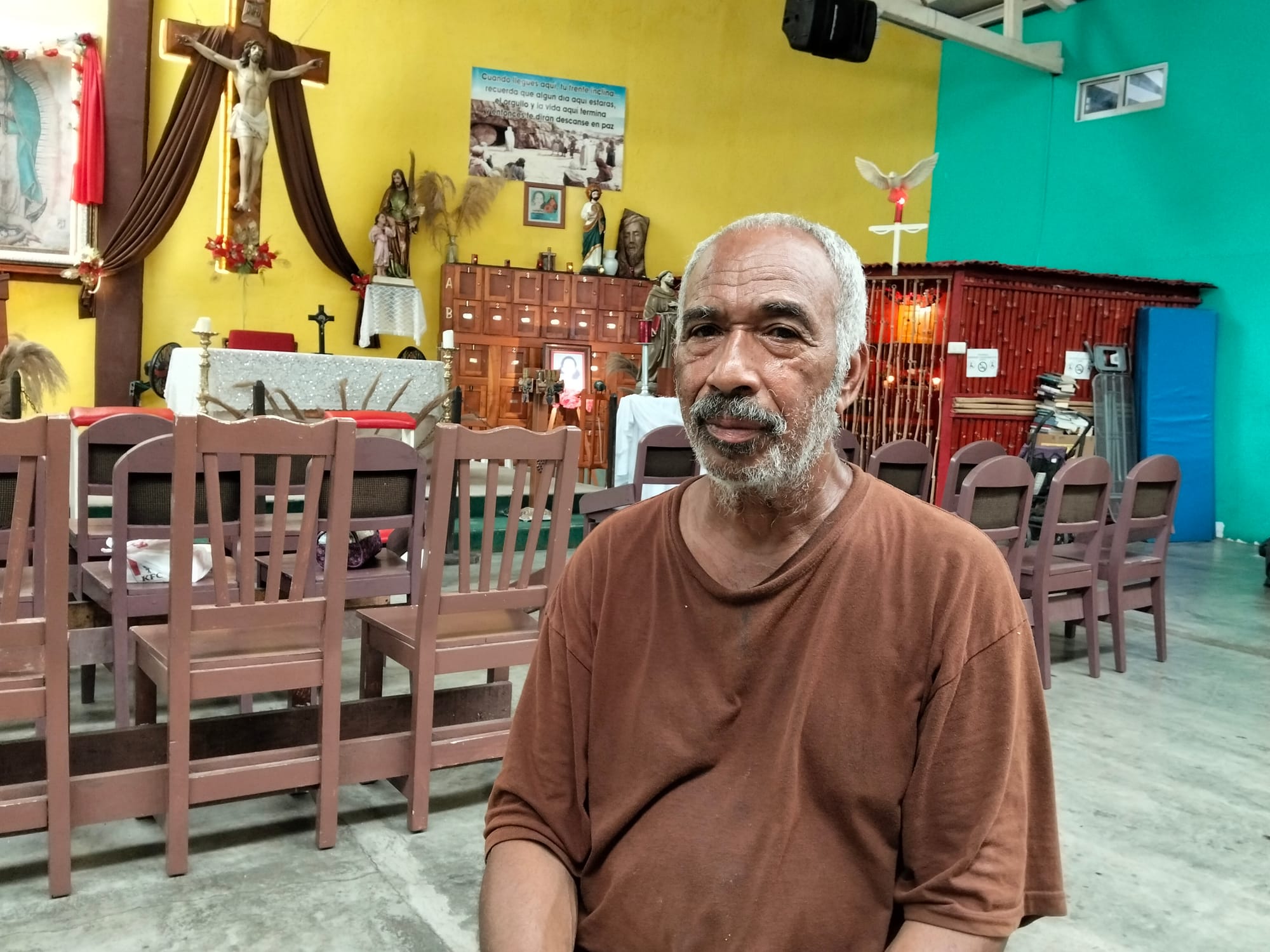 A man in a brown shirt sits in front of a yellow and turquoise wall
