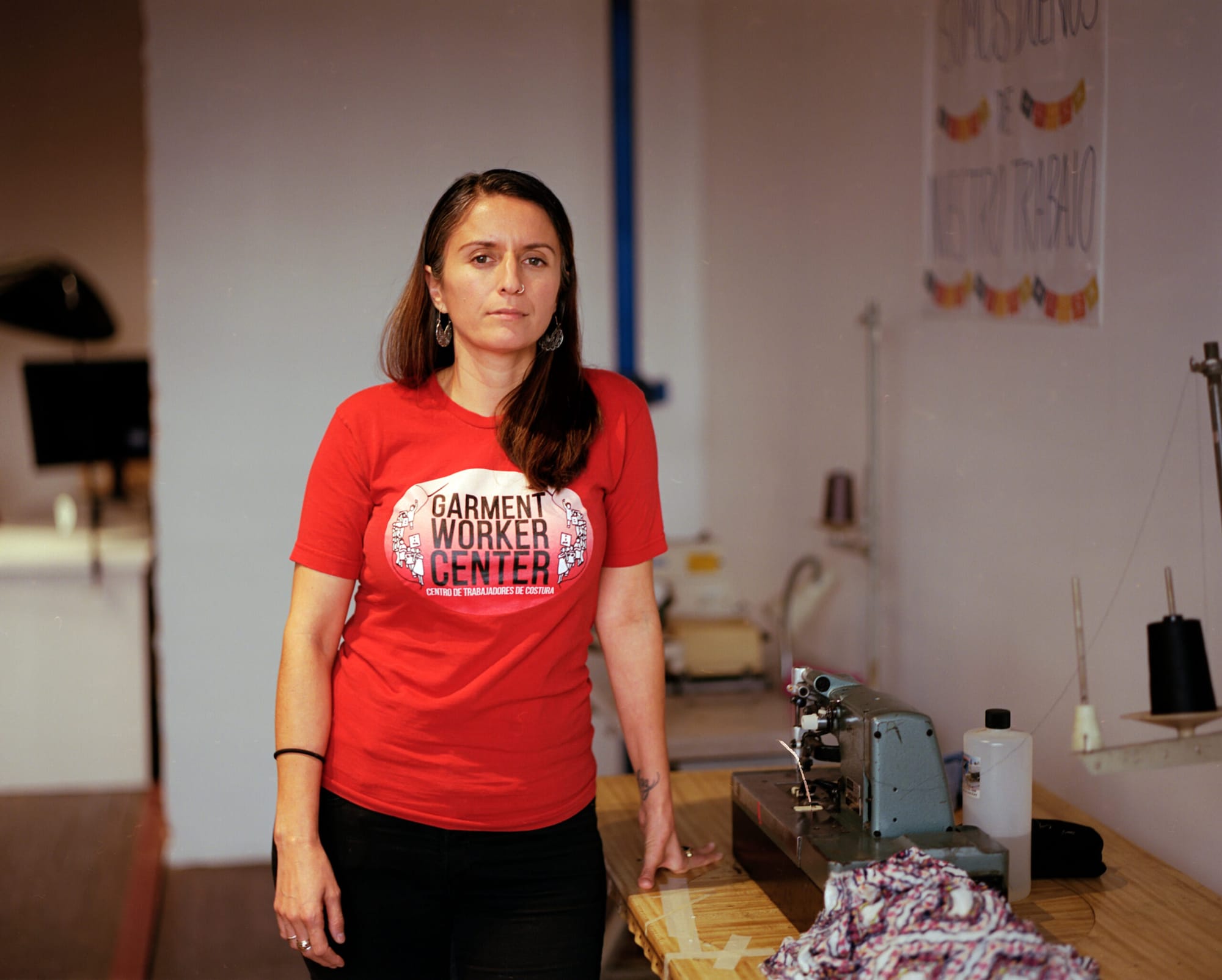 A woman in a red shirt poses next to a table with a sewing machine on it
