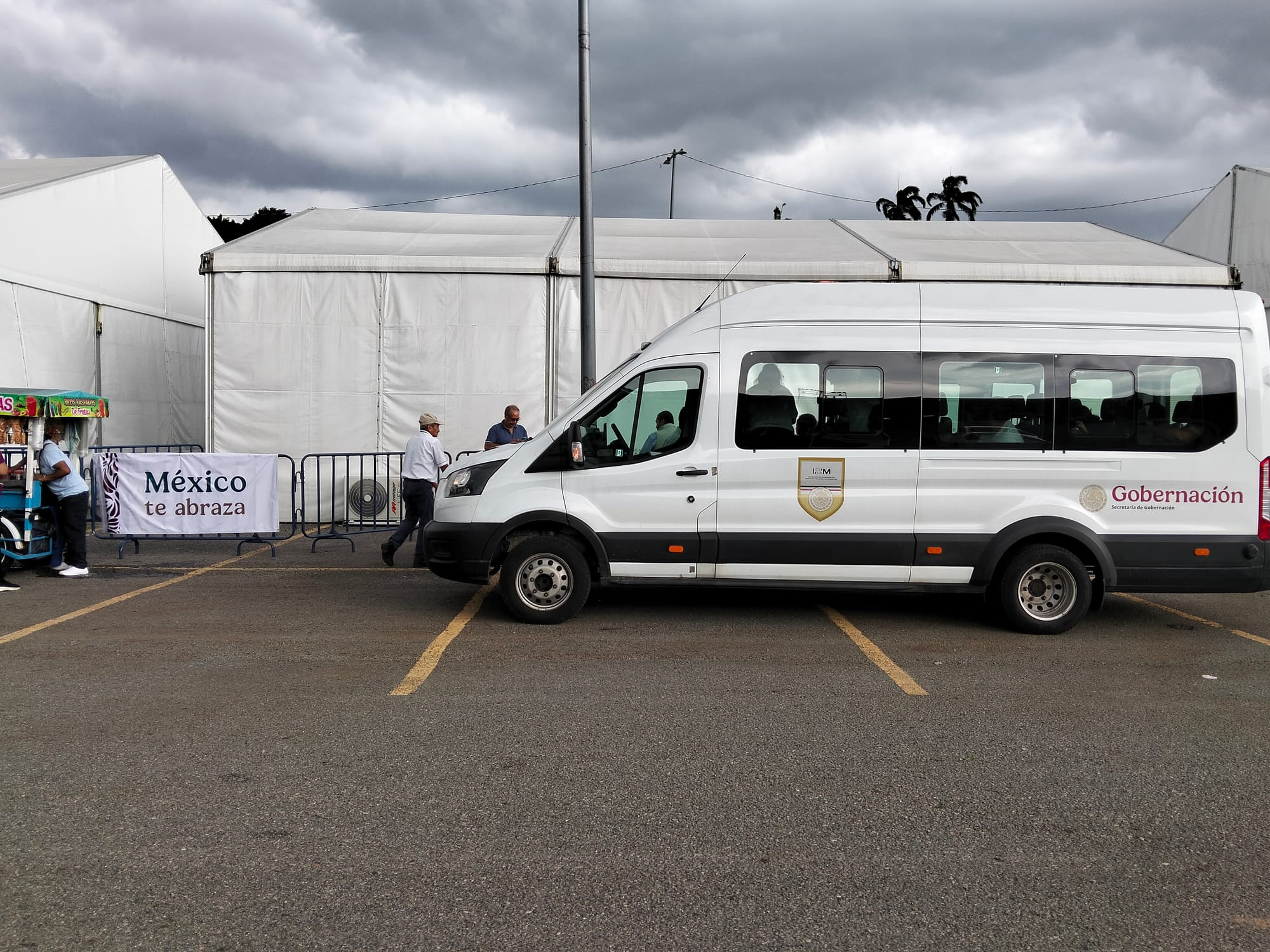 A white van in a parking lot in front of a tent.