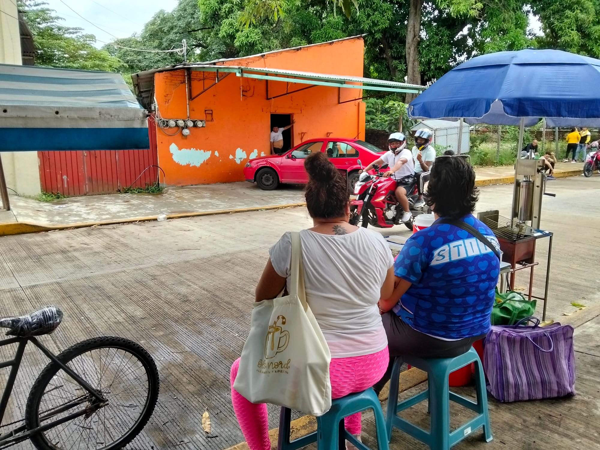 Two women sit facing away from the camera as a motorcycle passes them on the street