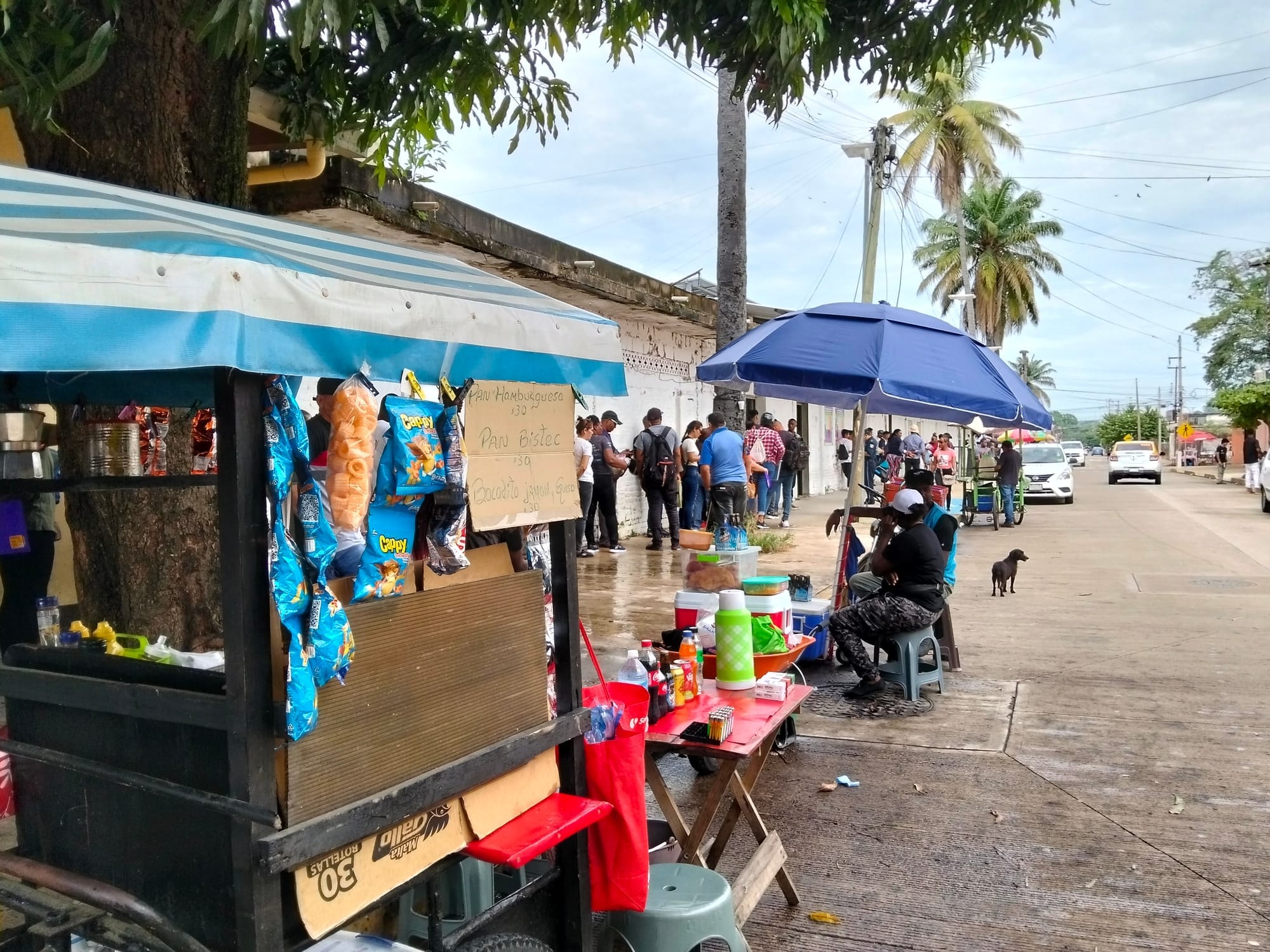 People stand in line outside a short building lined with business stands.