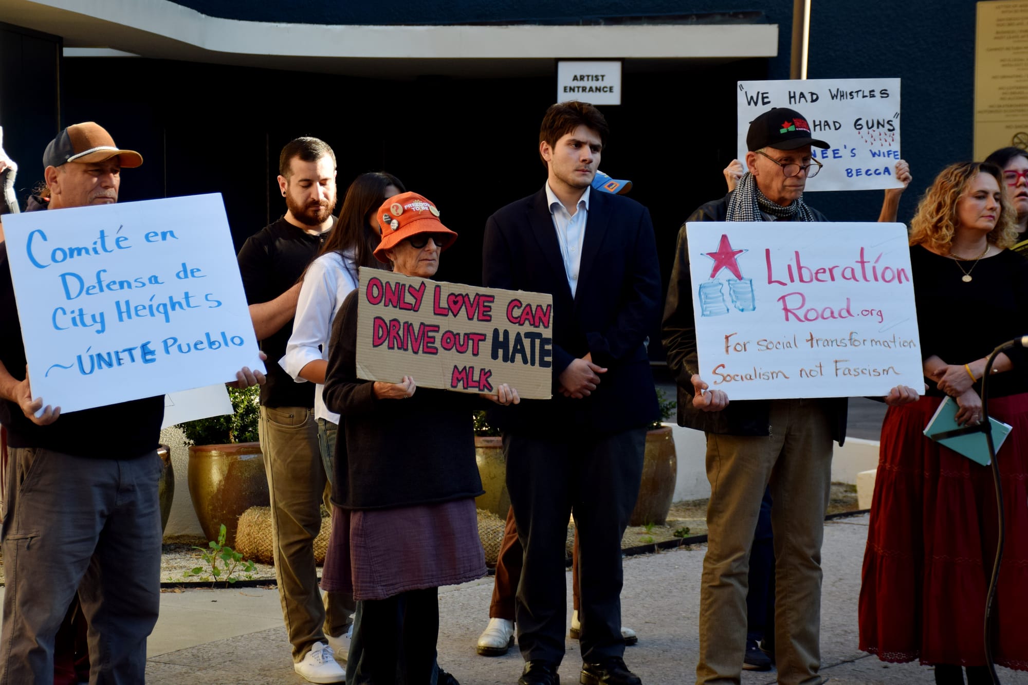 People stand outside holding signs, including one that says “Only love can drive out hate. MLK”