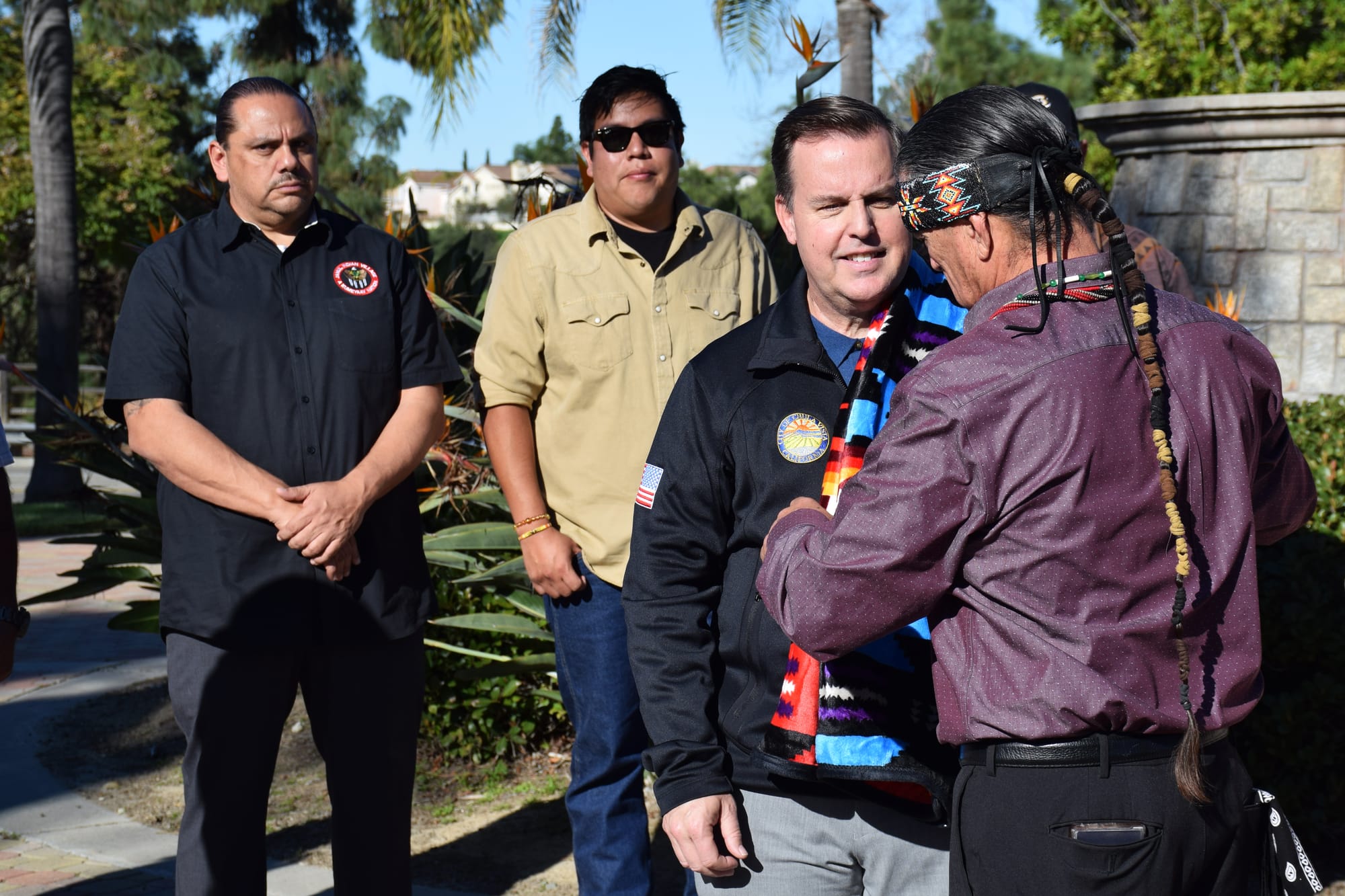 A man drapes another man with a blanket in an outdoor ceremony