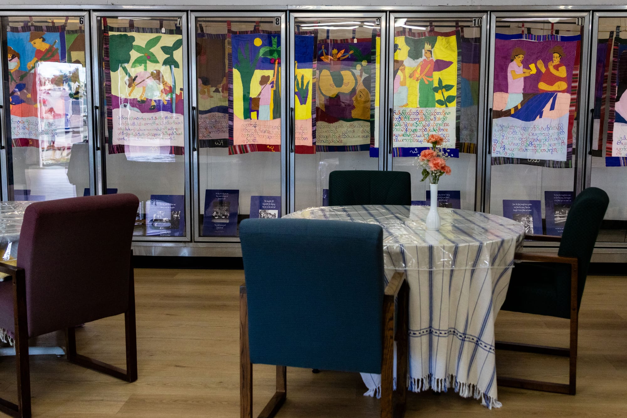Tables and chairs in front of a long fridge space that has art hanging in it.