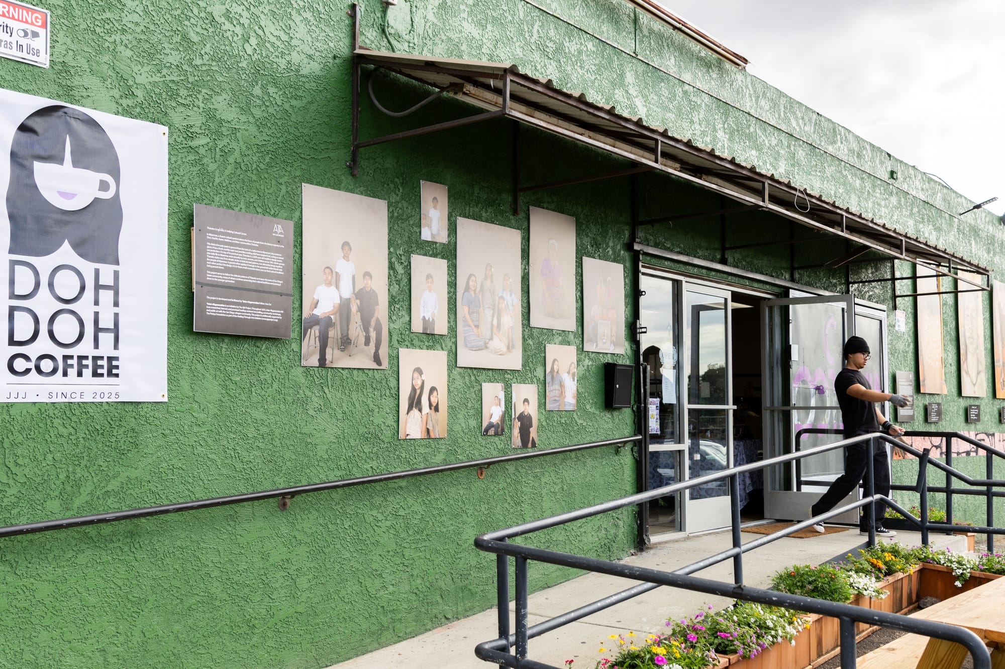 A man leaves a green building with art and a coffee shop sign.