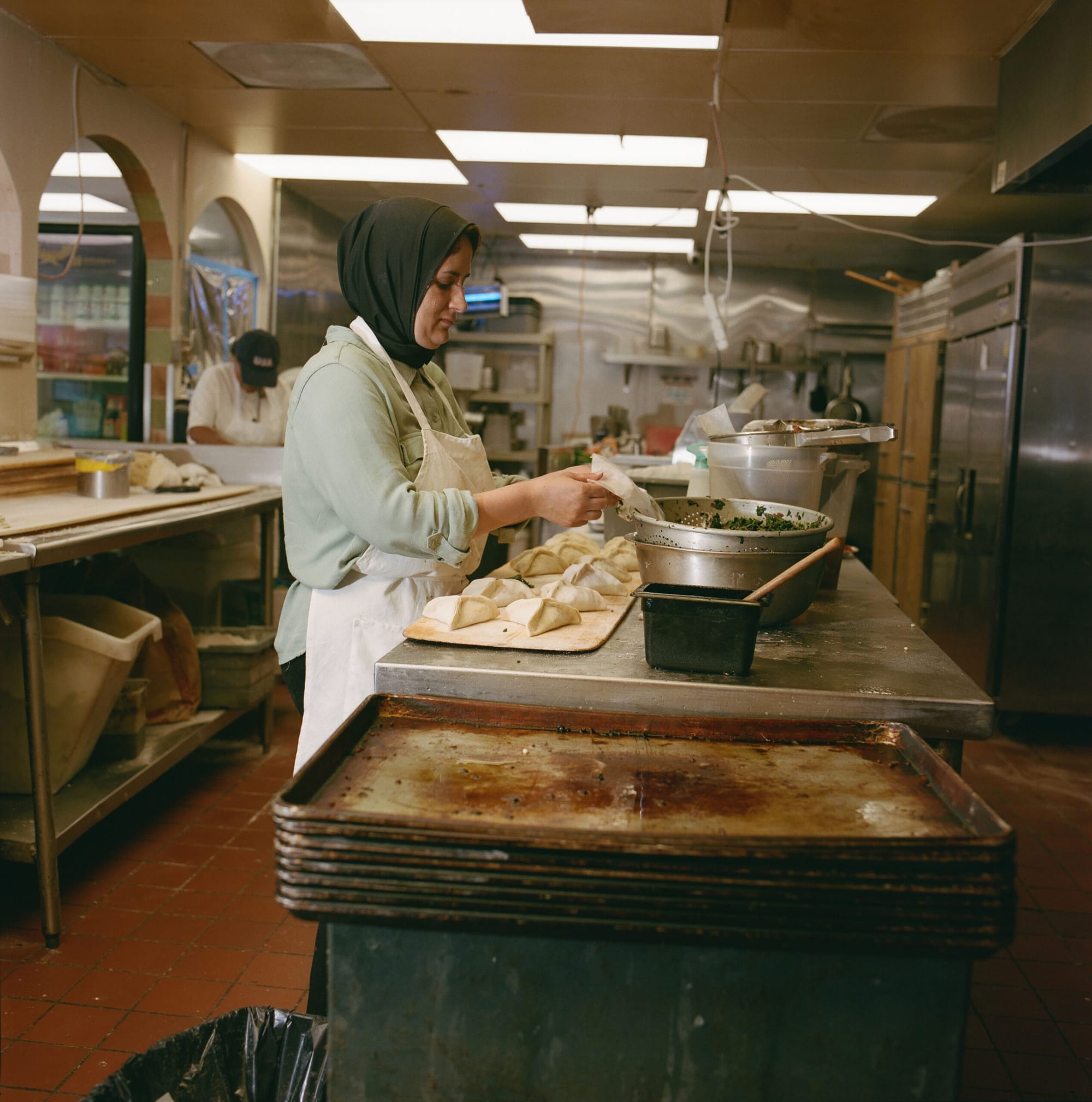 A woman in hijab stuffs pastries with a filling in a restaurant kitchen.