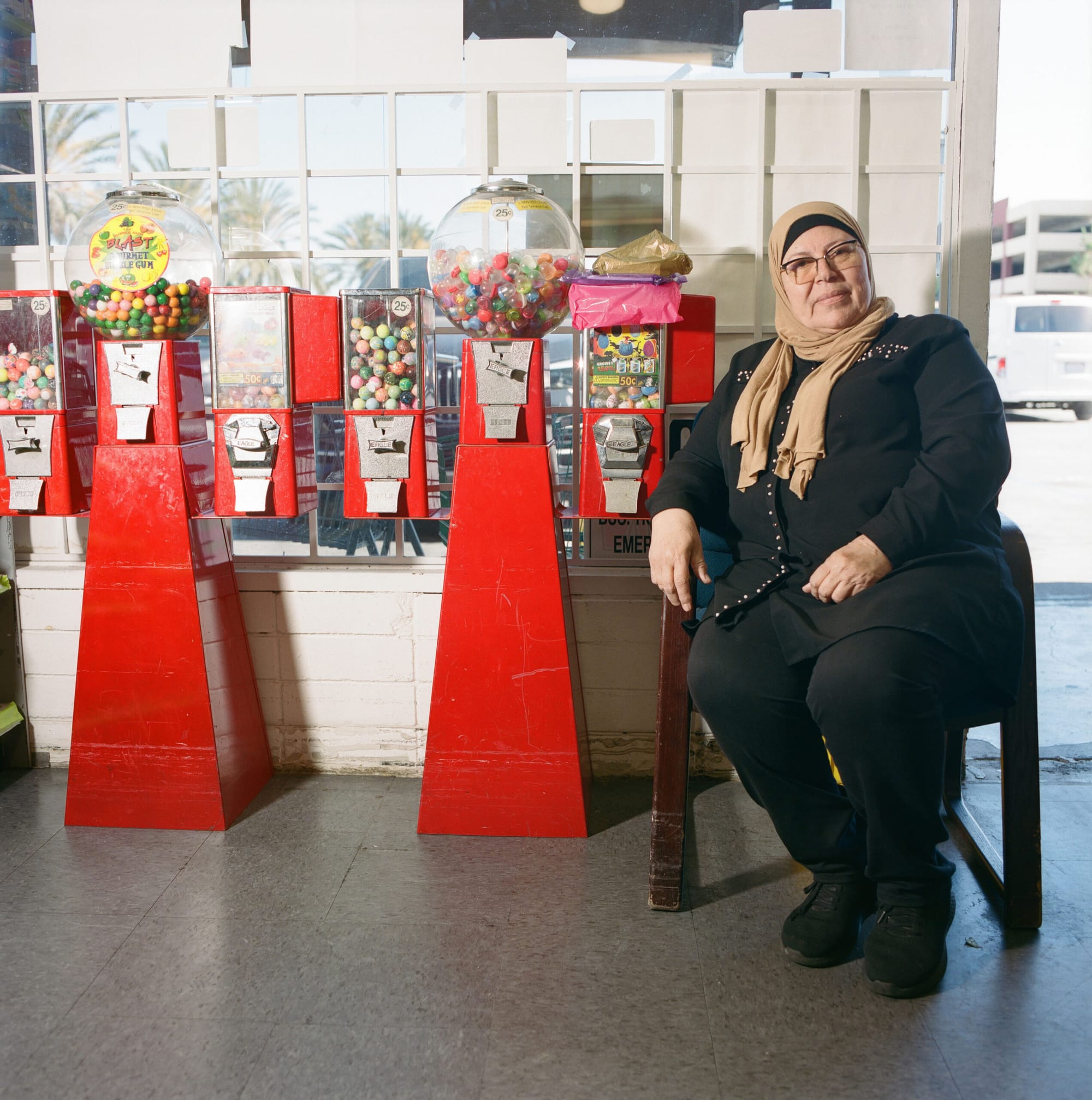 A woman in hijab sits next two a row of candy machines