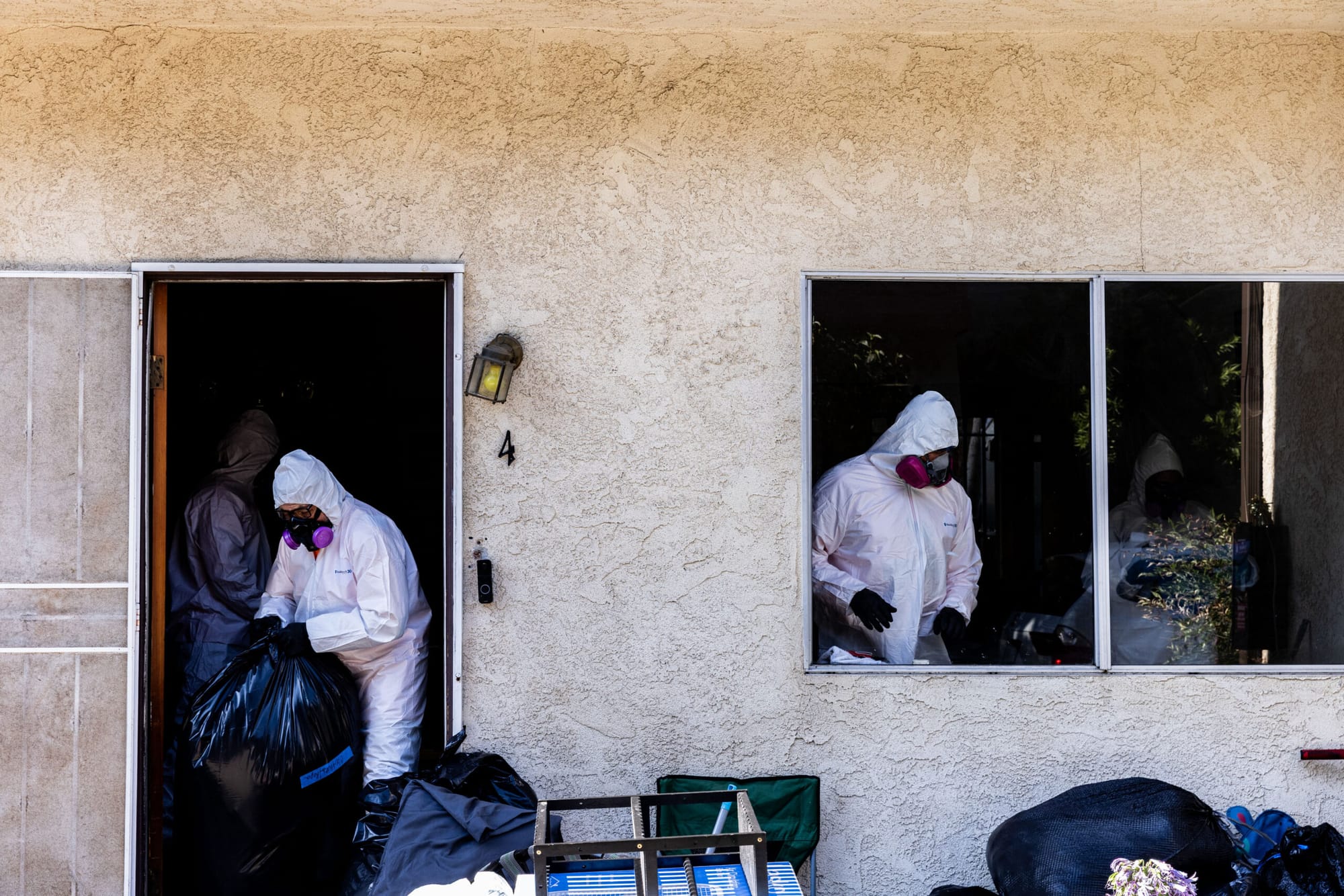 Four people wearing personal protective equipment can be seen cleaning an apartment through the doorway and window